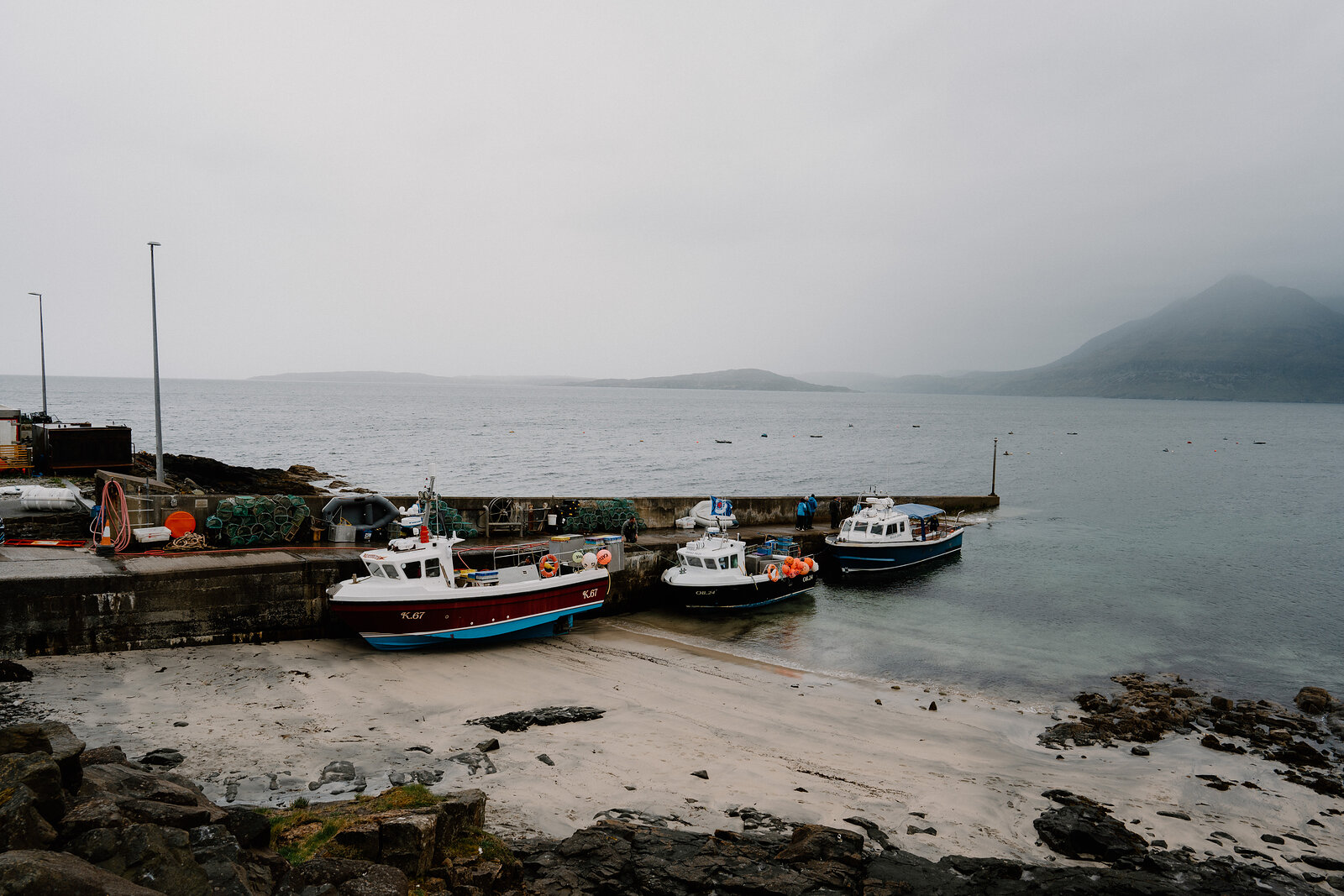 Fishing boats are moored at a stone slipway beneath a misty hillside on the Isle of Skye.