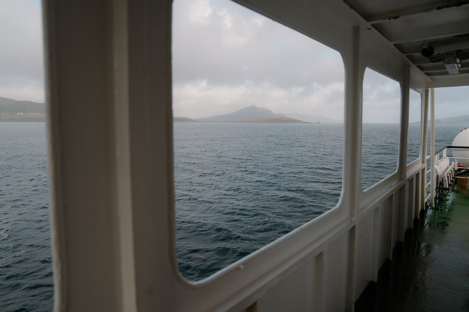 A misty hillside is framed by a ferry's window near the Isle of Skye.