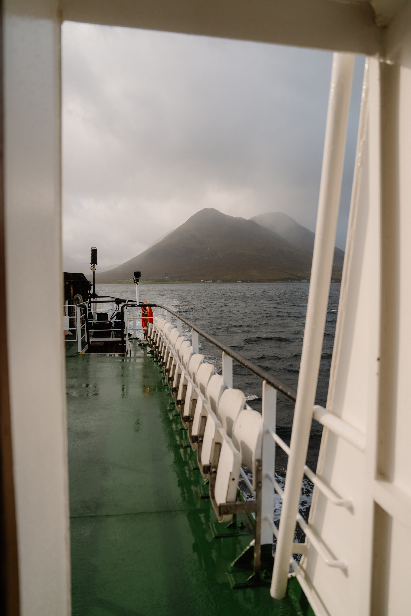 Folded seating lines a ferry deck framed by a doorway, with misty hills beyond near the Isle of Skye.