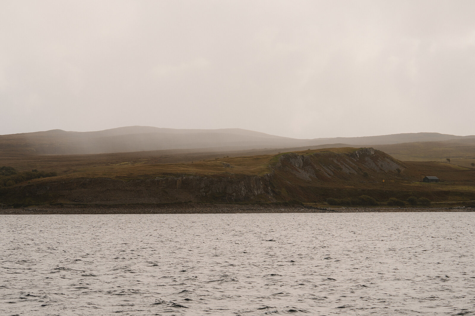 Mist drifts over a grassy headland seen from the water near the Isle of Skye.