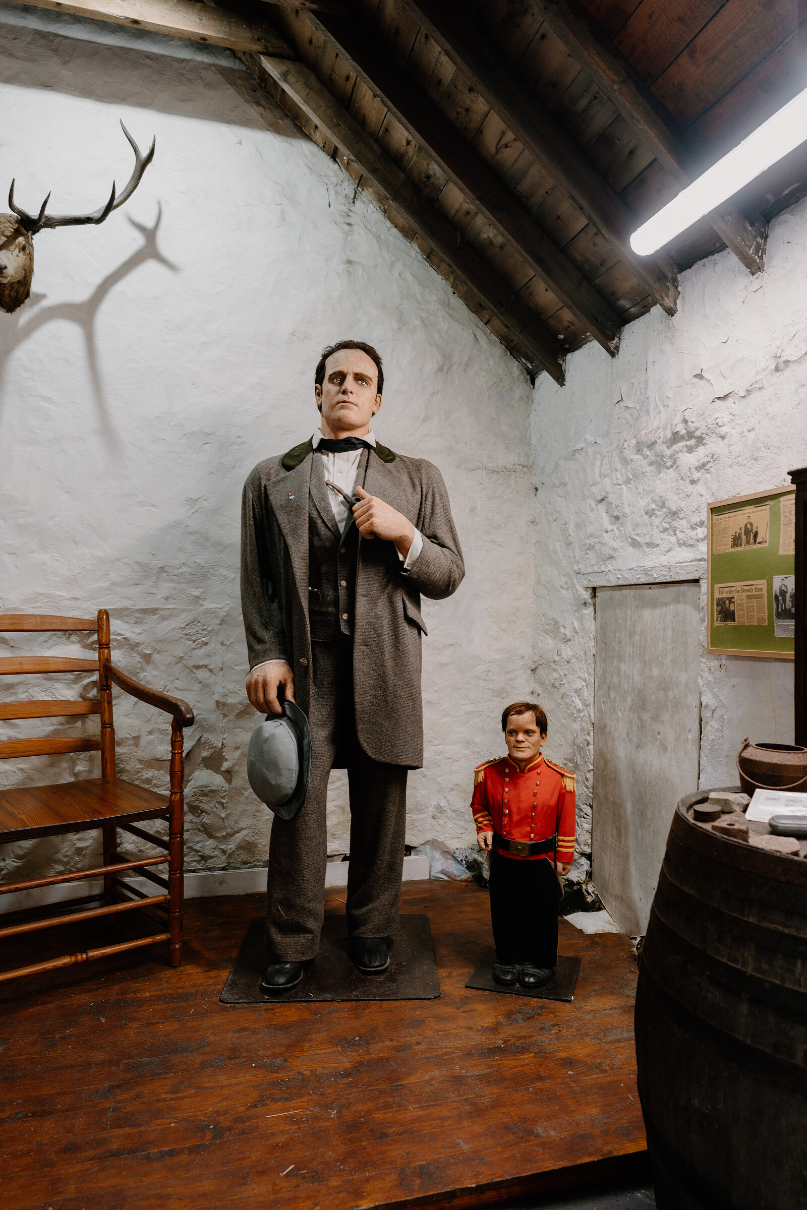 A giant mannequin towers over a smaller uniformed figure beneath mounted antlers inside the Giant Angus MacAskill Museum, Isle of Skye.