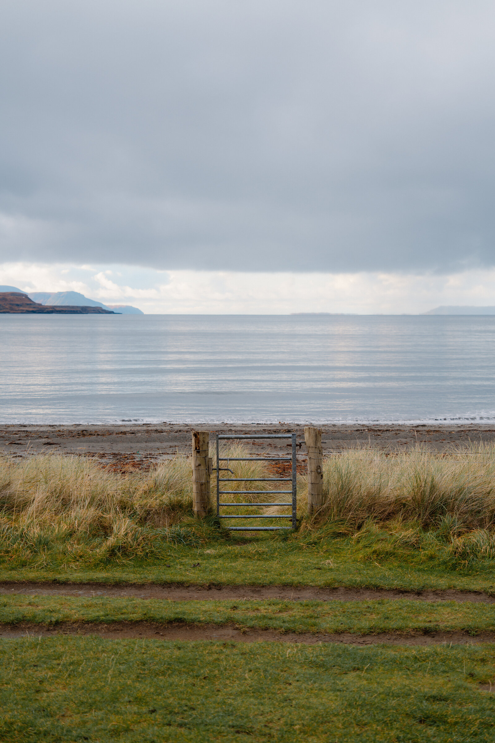 A metal farm gate overlooks a calm sea and distant islands near Glenbrittle, Isle of Skye.