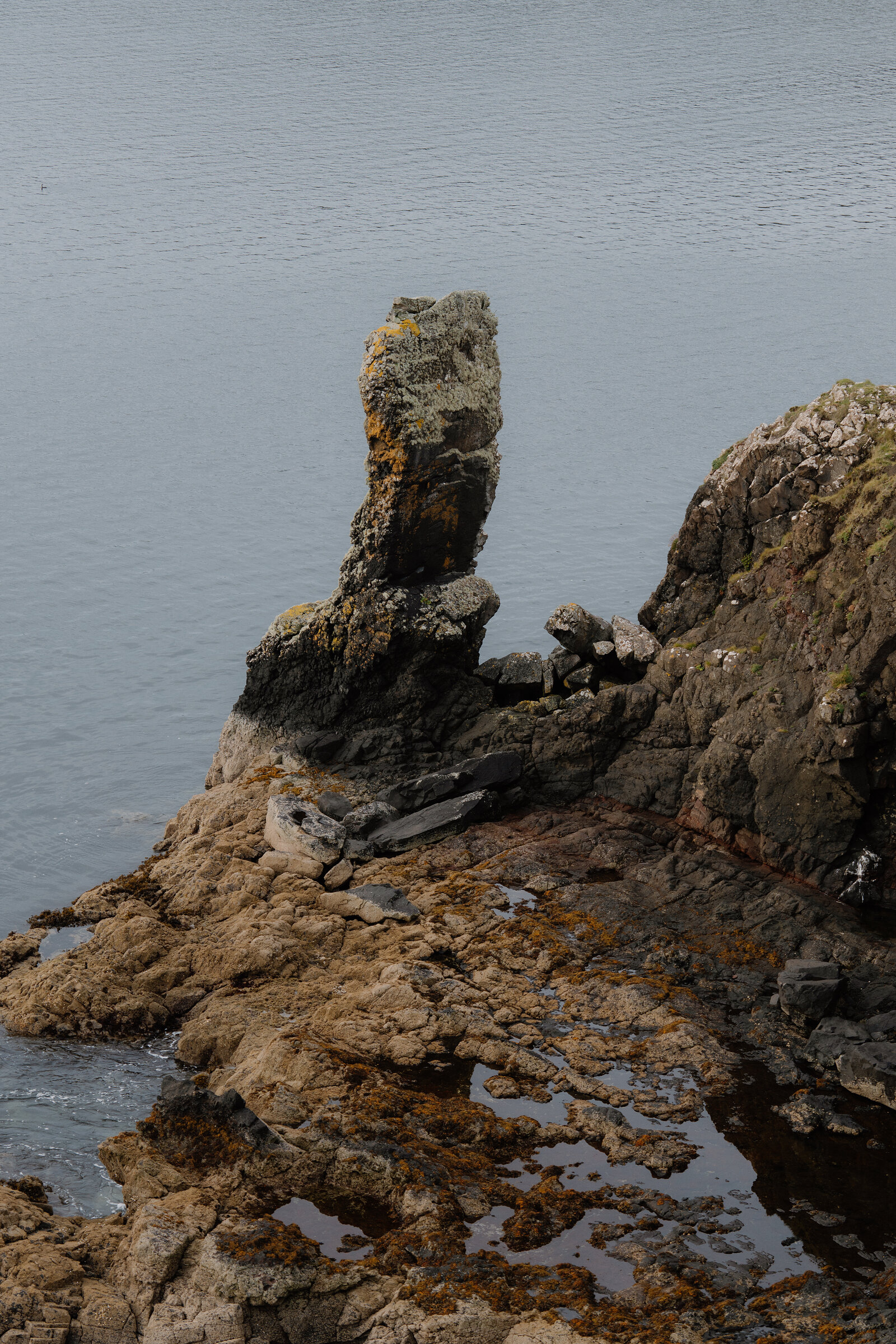 The weathered pillar of rock at the point, lichen on its face and rock pools at its foot.