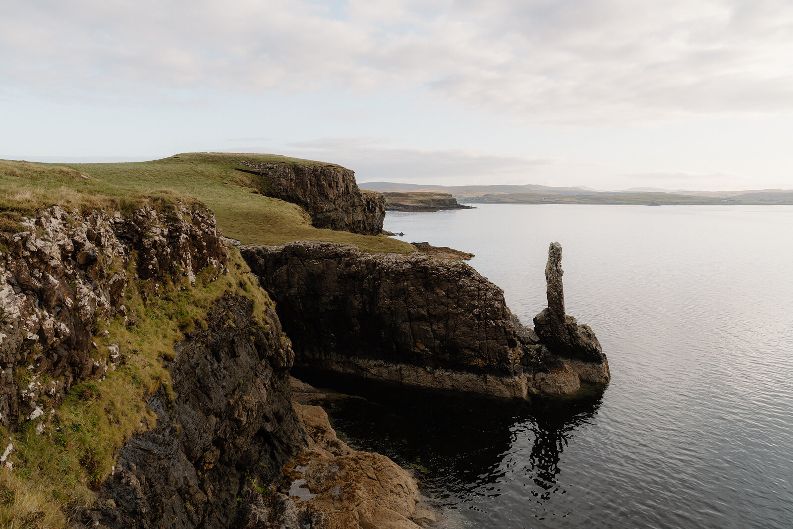 A rock pillar catches evening light beside cliffs on the Isle of Skye.