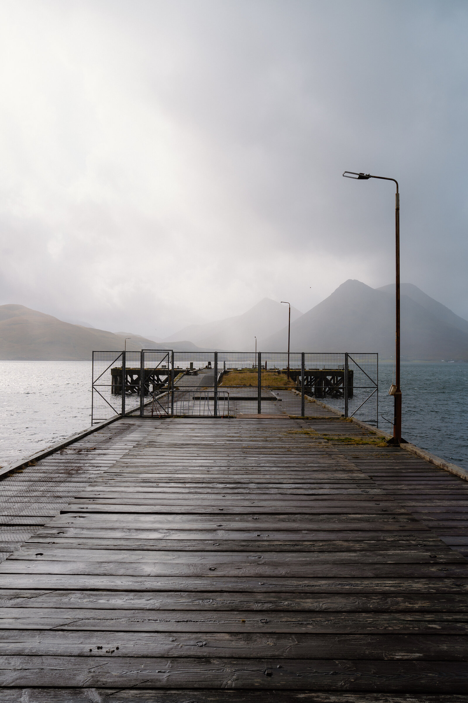 A wooden jetty with metal gates stretches into misty water beneath mountains on the Isle of Skye.