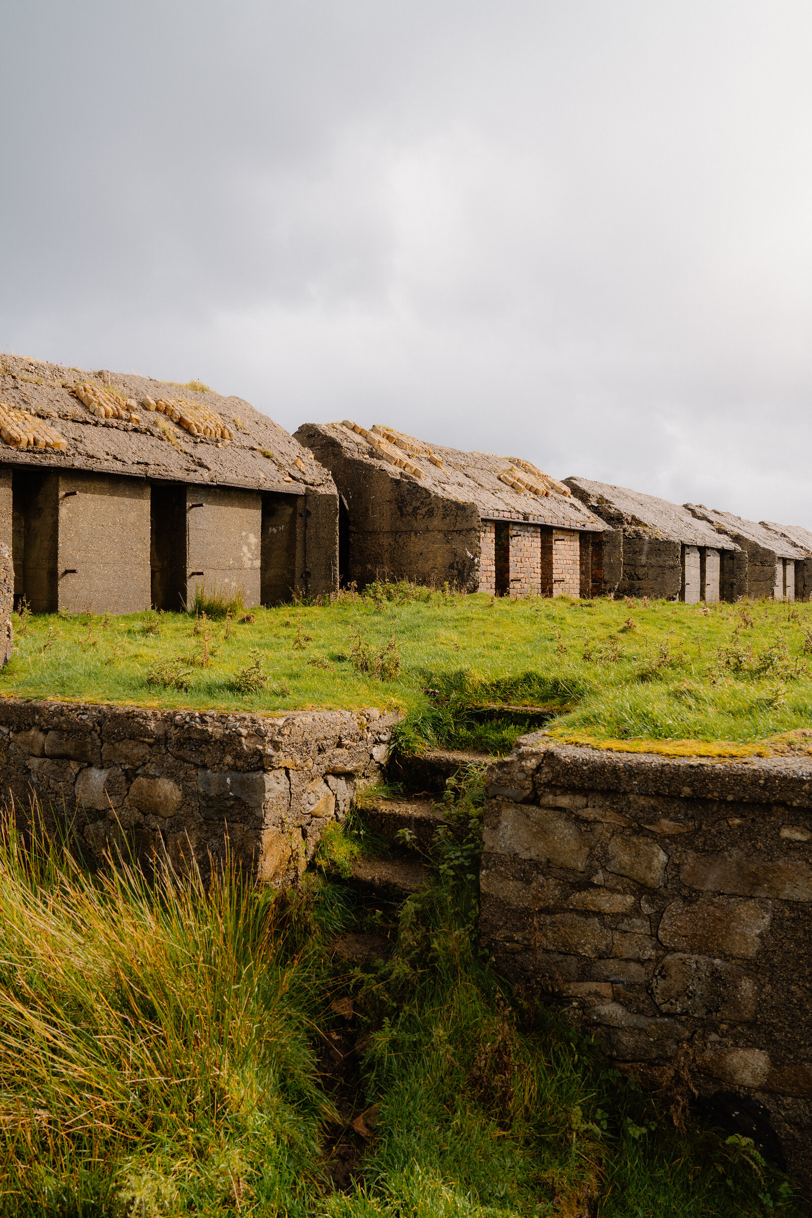 A row of turf-roofed concrete kiln structures lines a grassy hillside on the Isle of Skye.