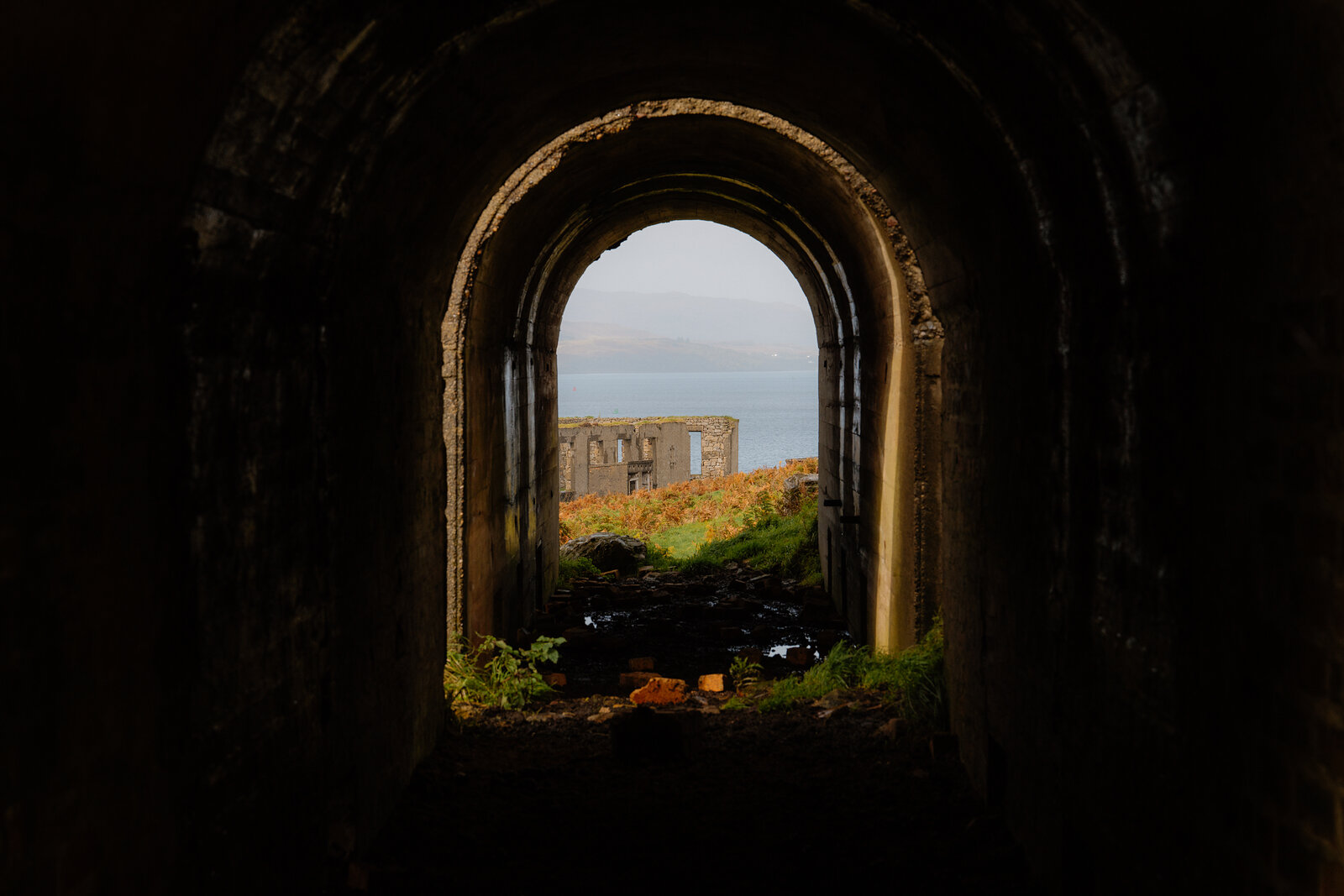 Autumn ferns surround a stone tunnel opening onto ruined buildings and the sea on the Isle of Skye.