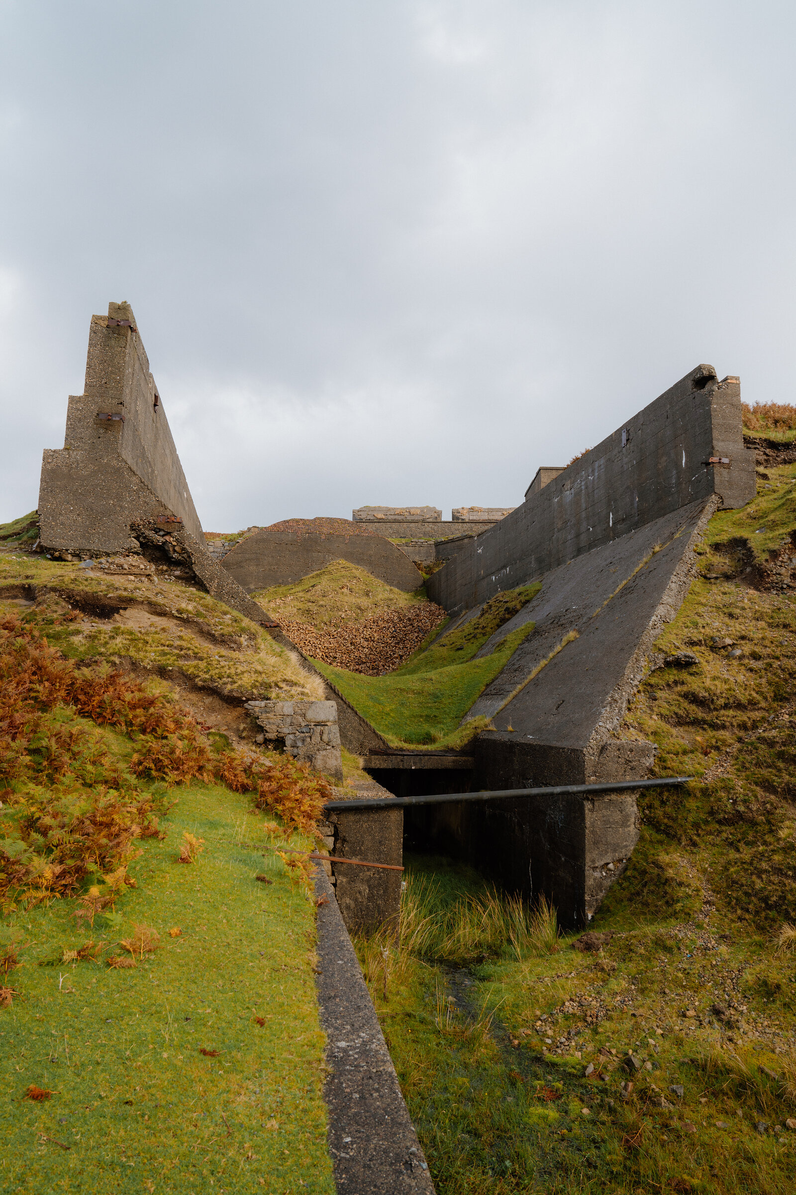 A concrete drainage channel runs between angular ruined structures on the Isle of Skye.