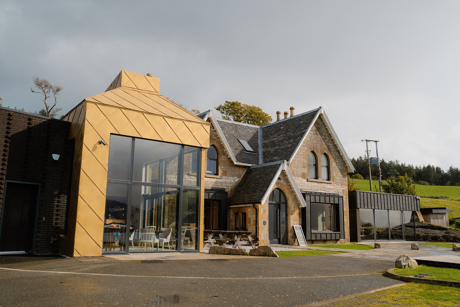 A gold-clad extension joins a stone mansion at the Isle of Raasay Distillery, a whisky barrel on the lawn.
