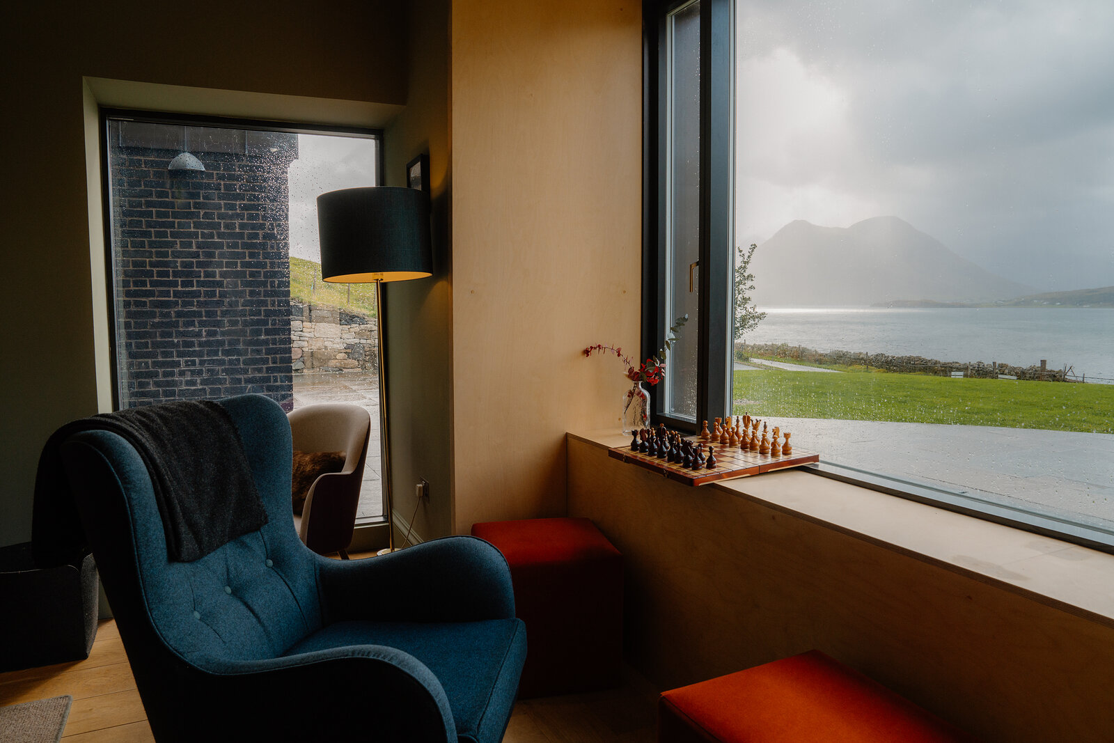 A chess set sits on a window ledge beside a teal armchair overlooking the Cuillin at the Isle of Raasay Distillery.
