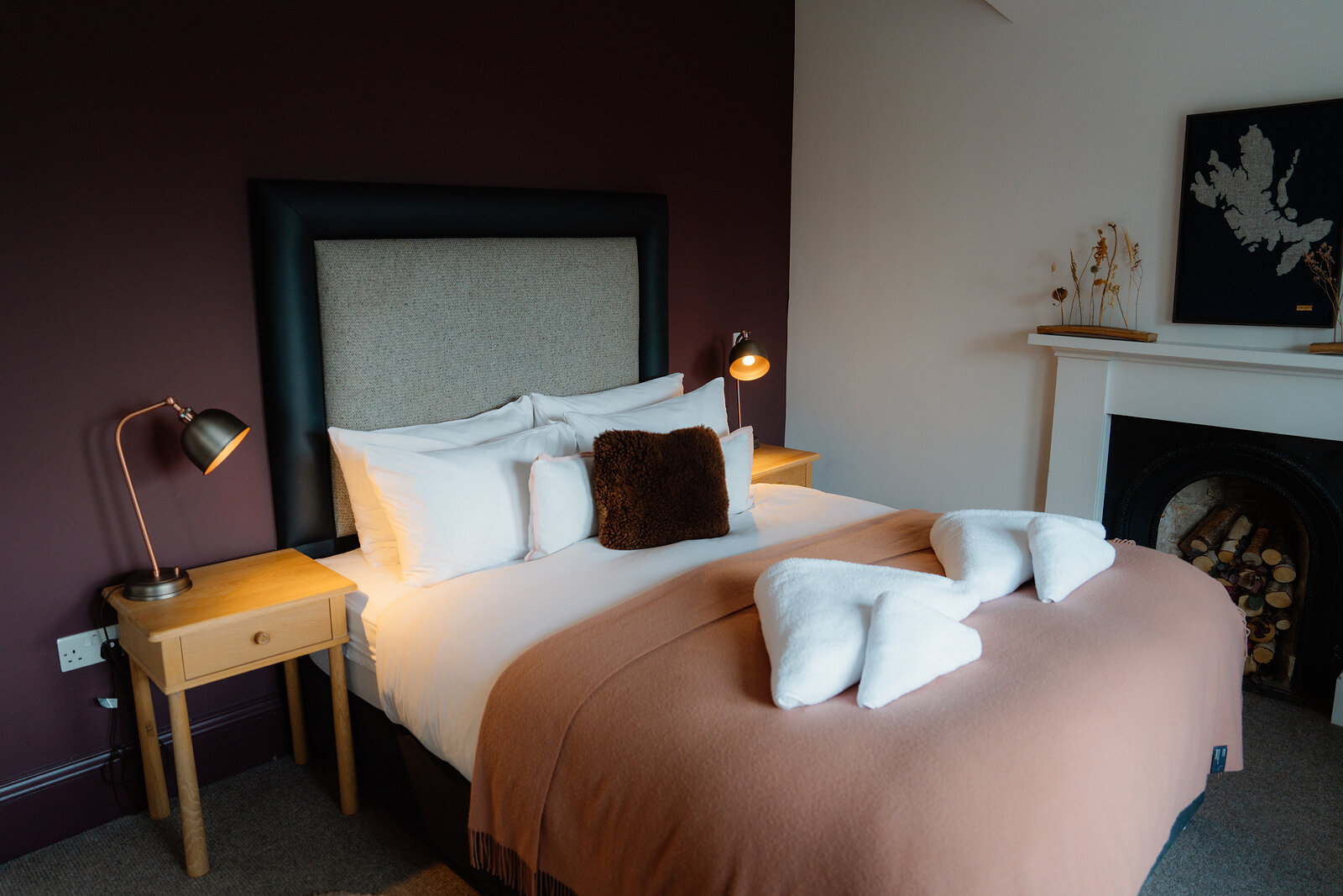 Swan-folded towels sit on a bed beside a fireplace in a guest room at the Isle of Raasay Distillery.