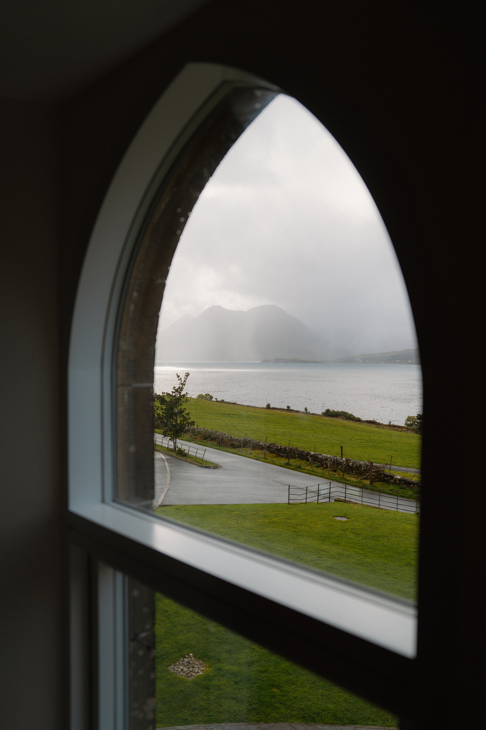 An arched window frames a misty loch and mountains at the Isle of Raasay Distillery.