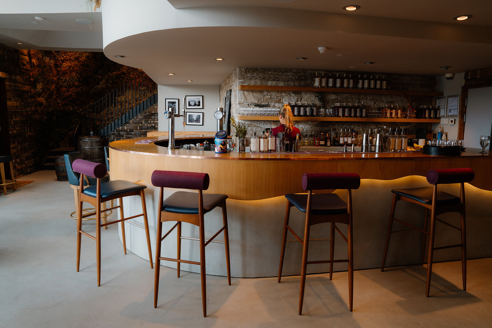 Purple velvet stools line a curved wooden bar at the Isle of Raasay Distillery.