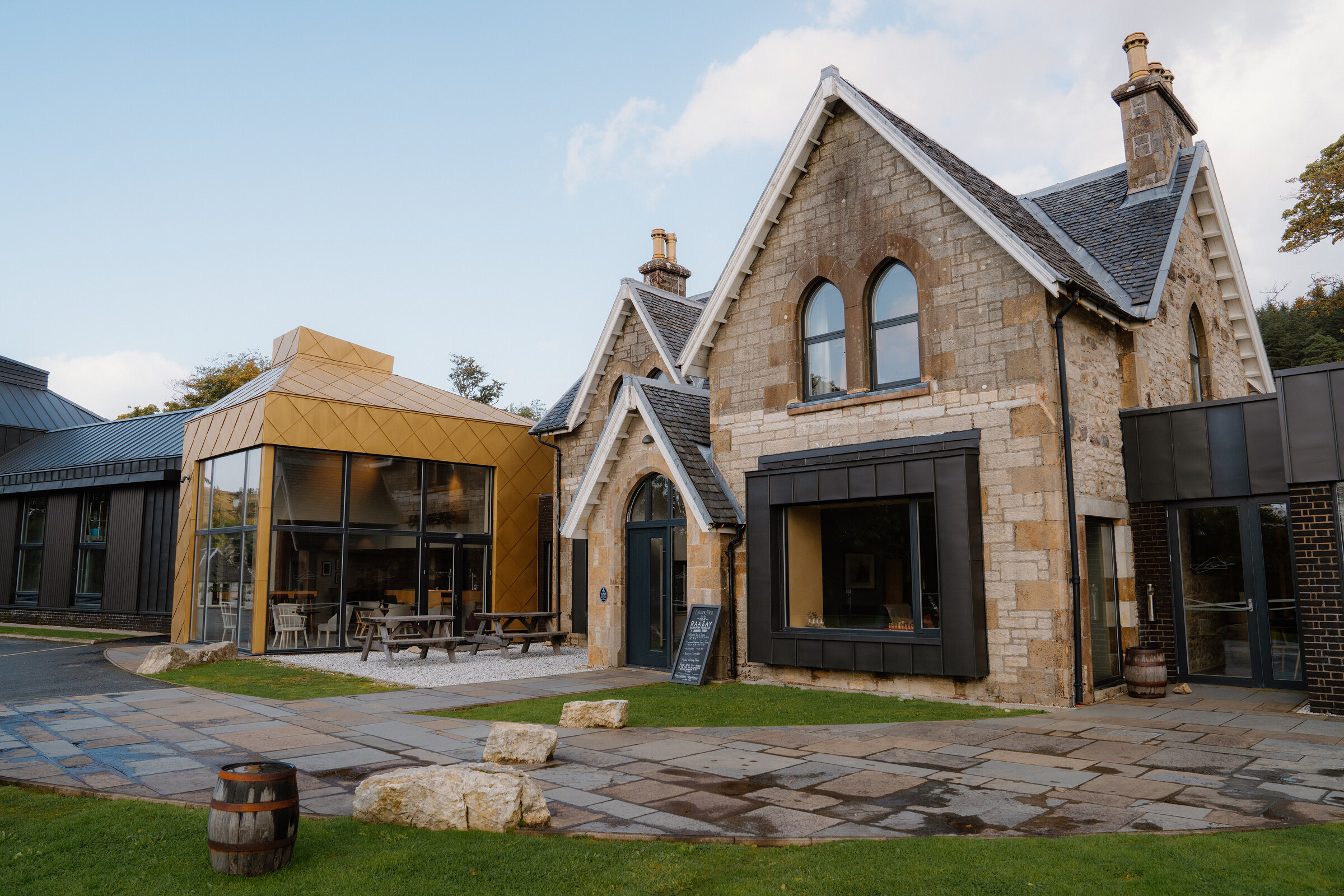 The Isle of Raasay Distillery's stone mansion and gold-clad extension face a courtyard with picnic tables.