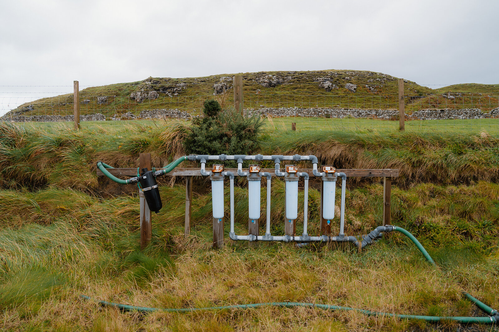 A row of filter canisters and hosepipes stands on a wooden frame in a field at the Isle of Skye Sea Salt Company.