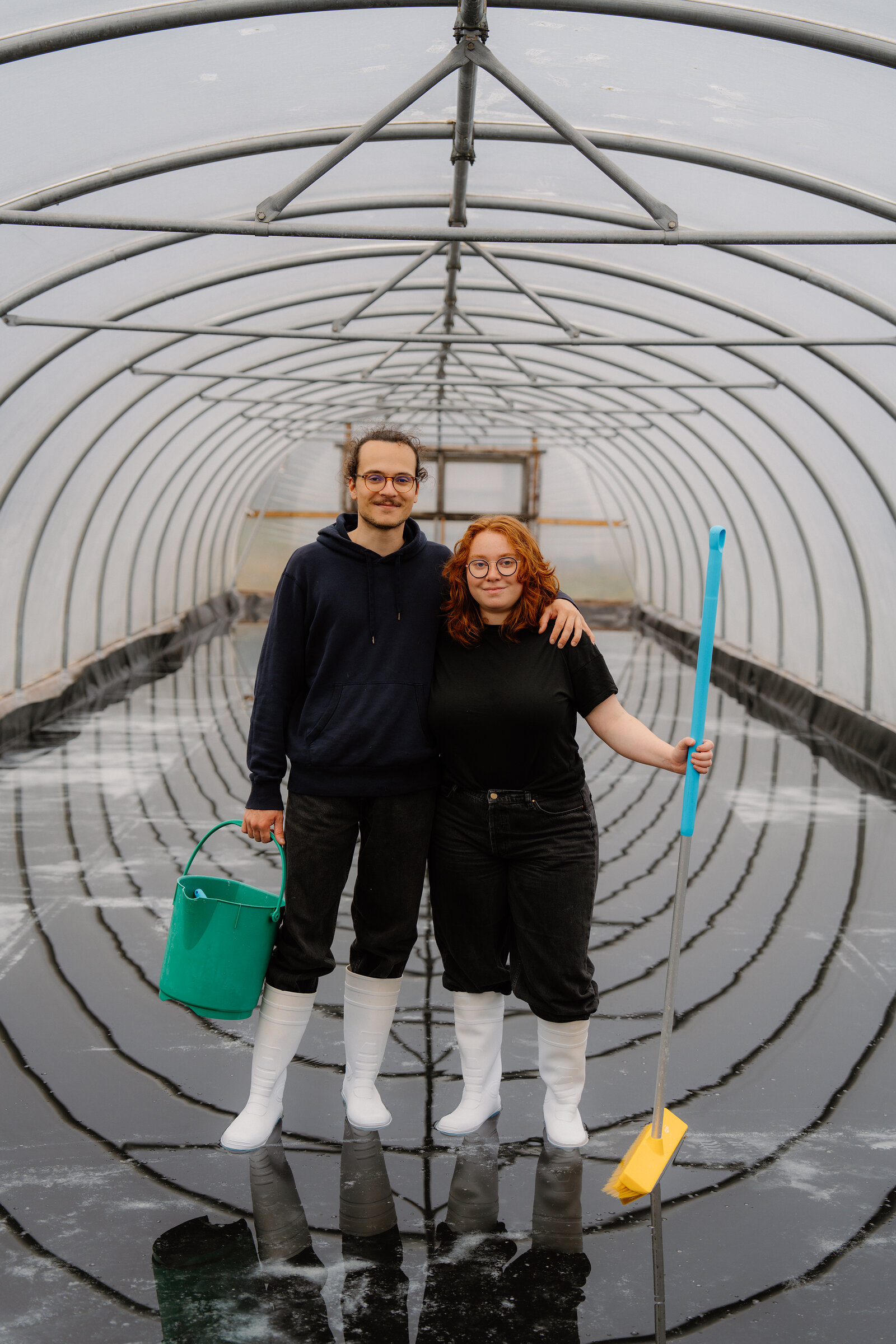 A man and woman in white boots pose together inside a flooded polytunnel at the Isle of Skye Sea Salt Company.