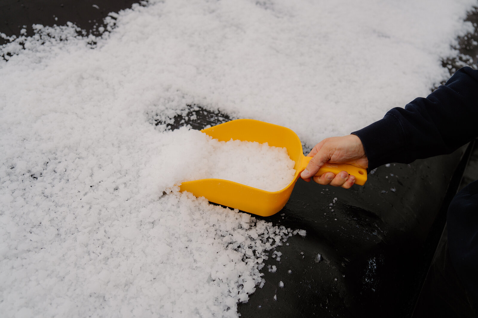 A hand scoops slushy sea salt with a yellow shovel at the Isle of Skye Sea Salt Company.