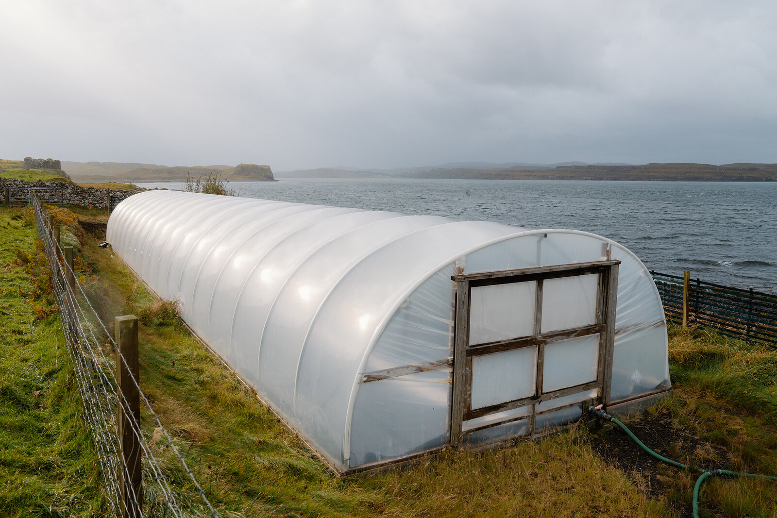 A polytunnel sits behind a stone wall above a sea loch at the Isle of Skye Sea Salt Company.