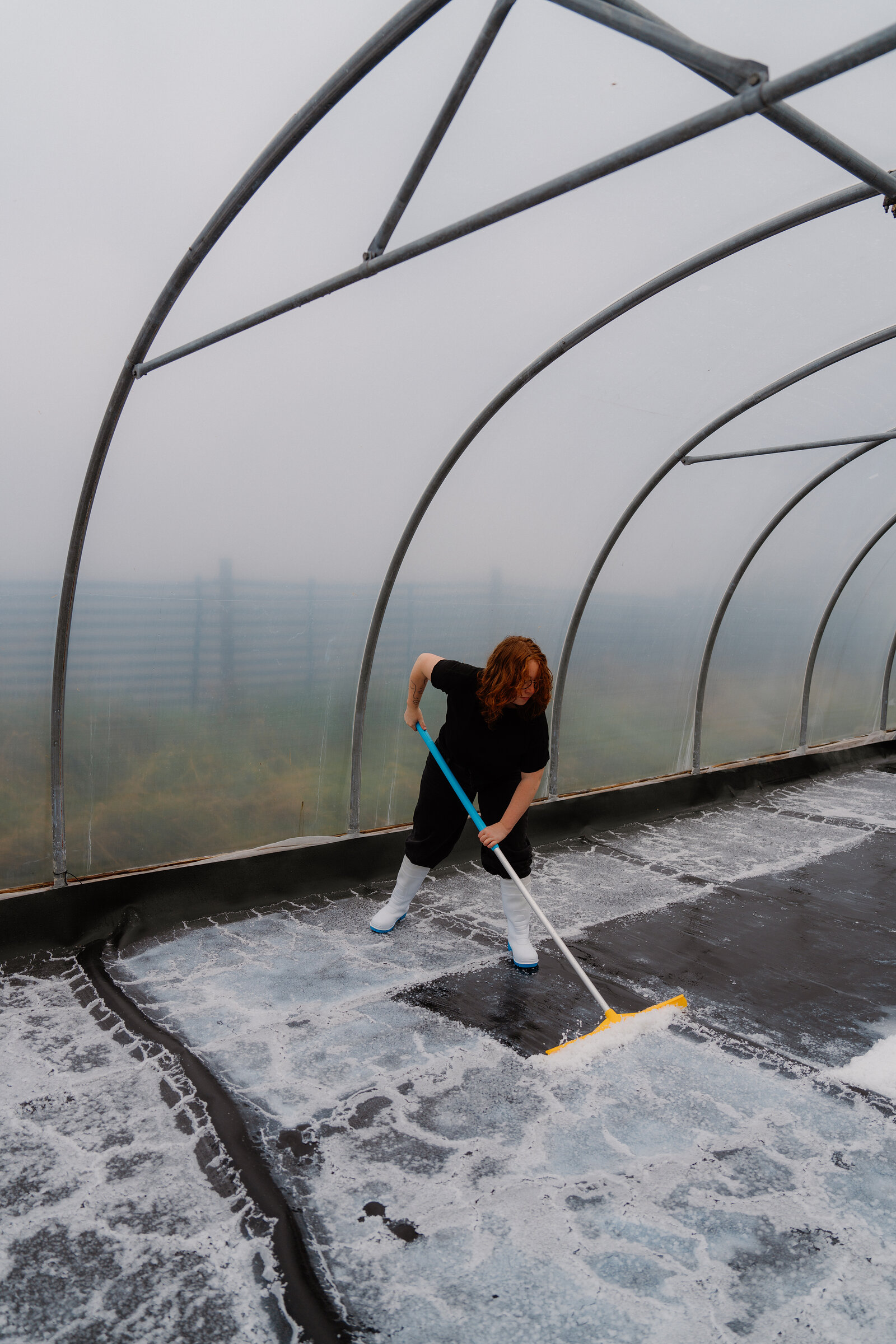 A woman sweeps salt with a long-handled squeegee inside a foggy polytunnel at the Isle of Skye Sea Salt Company.