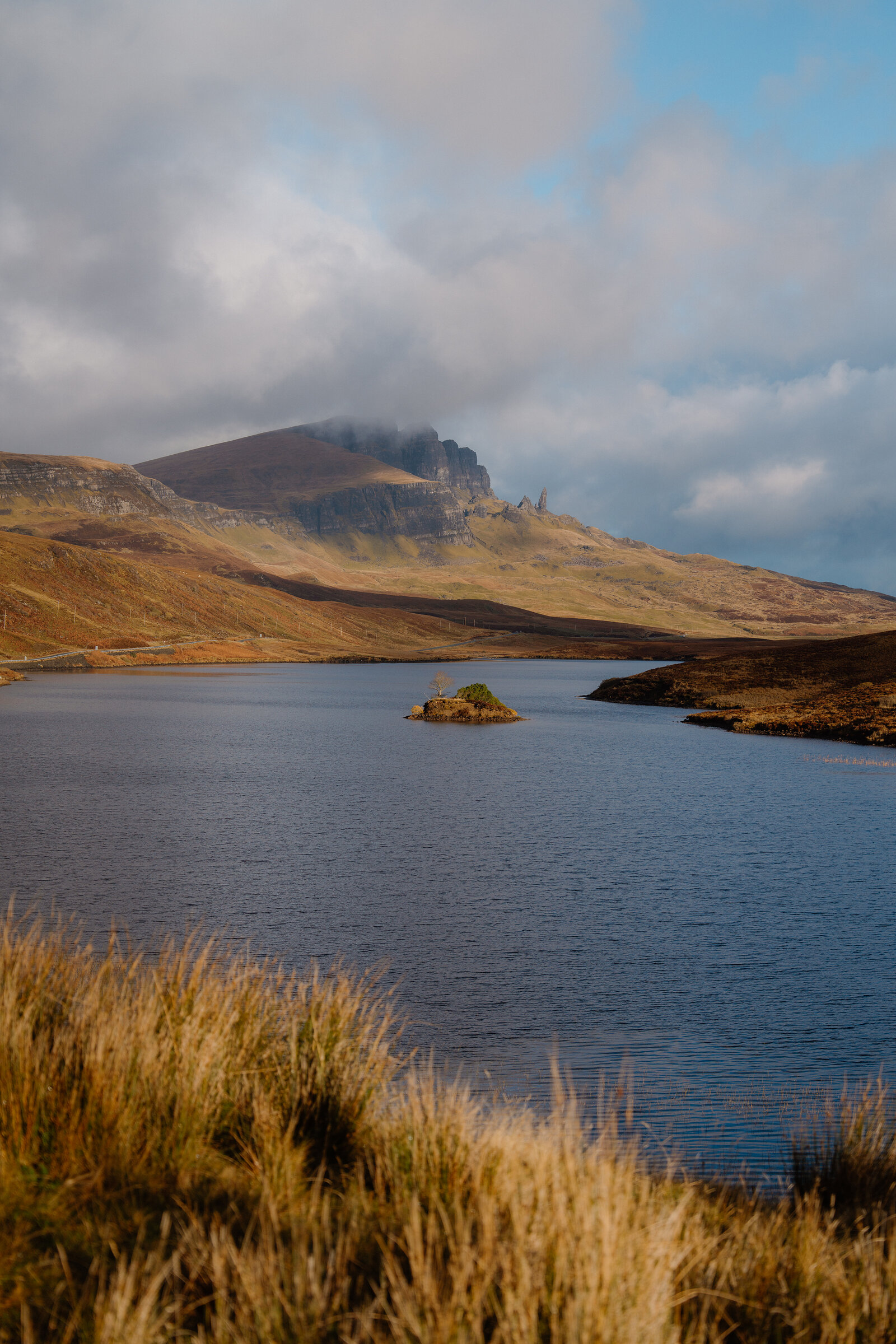 The Old Man of Storr's pinnacle rises through cloud above Loch Fada on the Isle of Skye, a small island in the water.