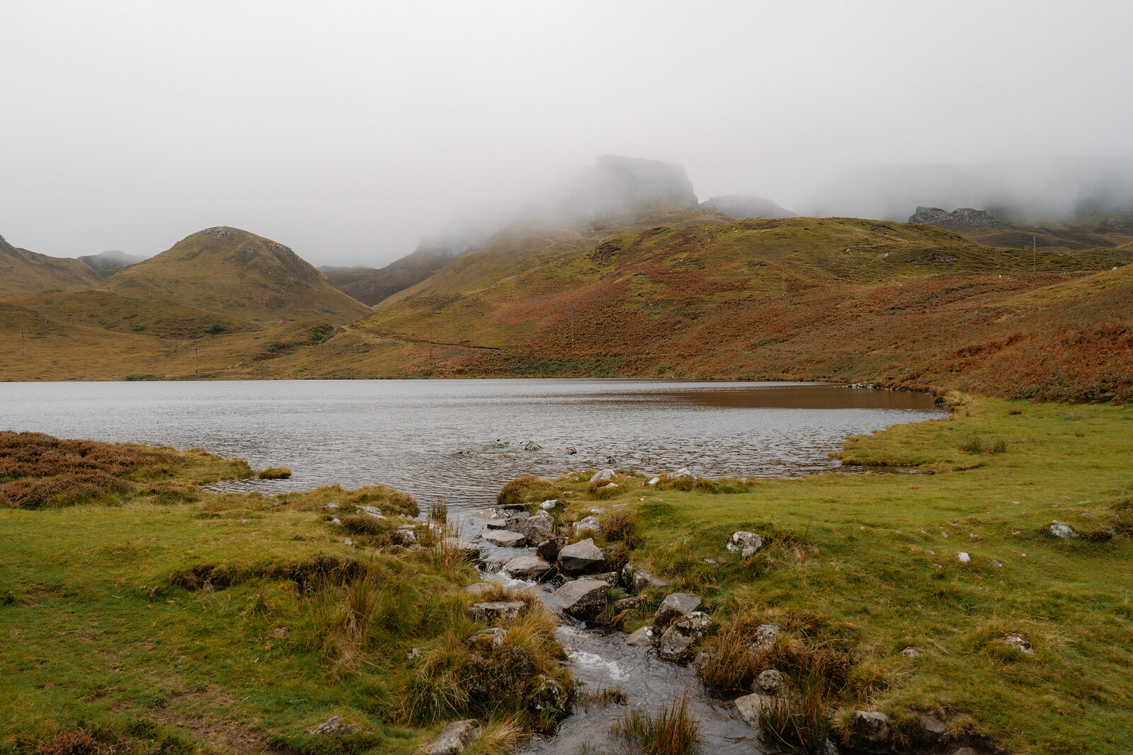 A stream feeds into a misty loch below a cloud-wrapped hillside on the Isle of Skye.