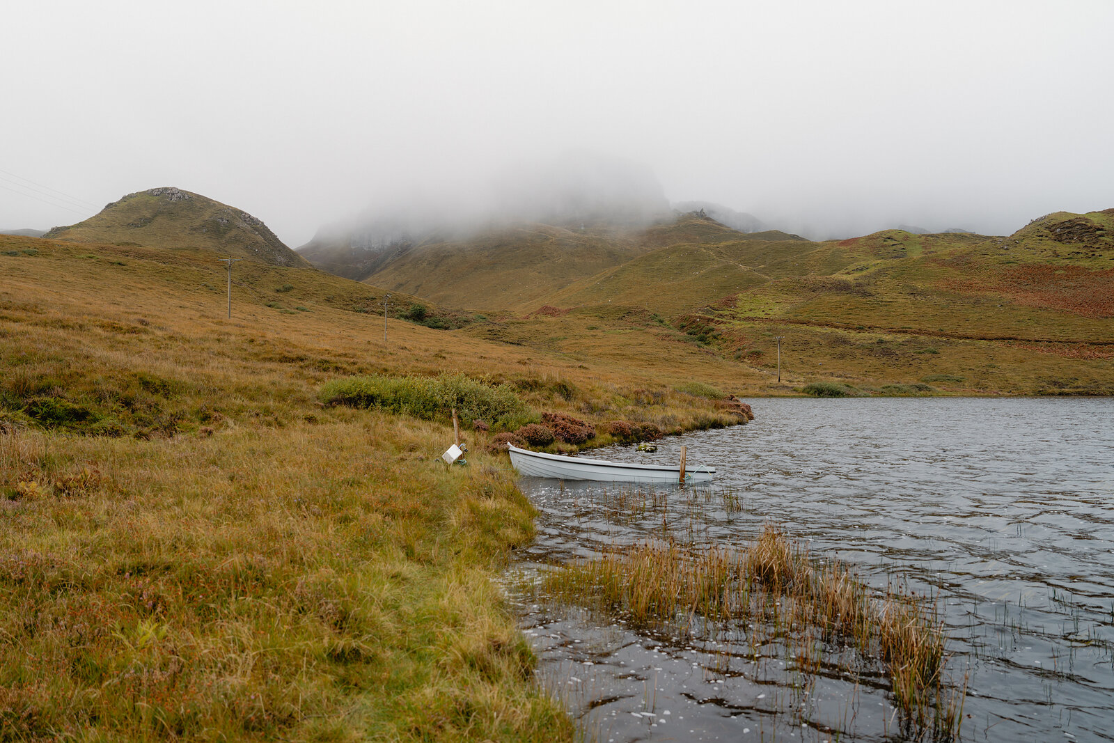 A small white boat is moored on a misty loch below cloud-wrapped hills on the Isle of Skye.