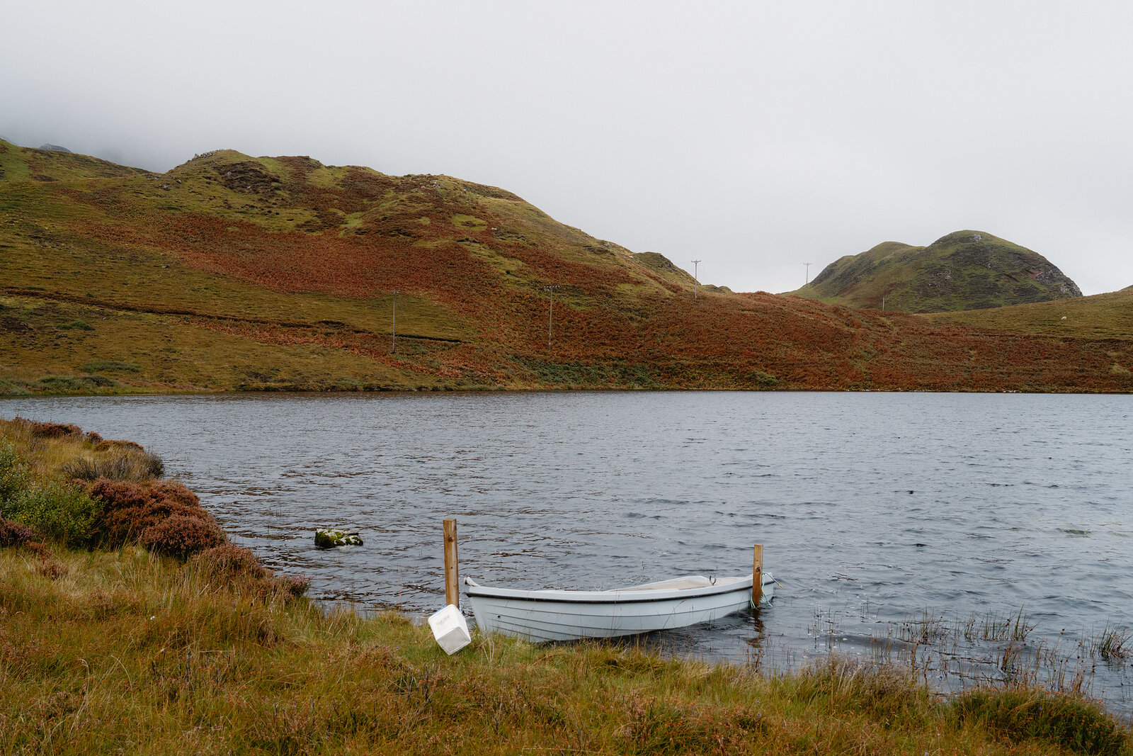 A white boat sits moored at the edge of a loch surrounded by autumn-toned hills on the Isle of Skye.