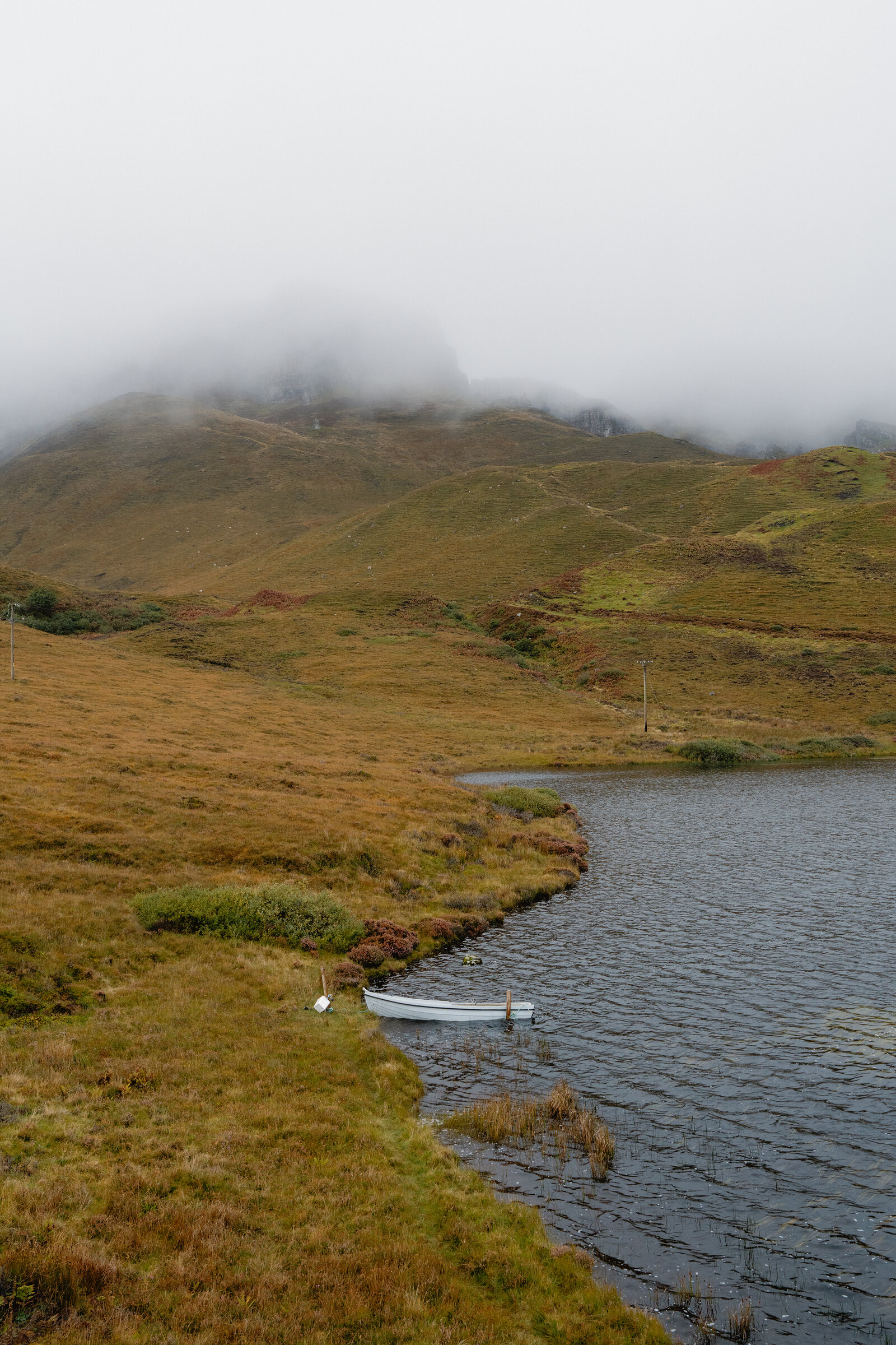 A small boat is moored on a loch beneath a mist-shrouded hill on the Isle of Skye.