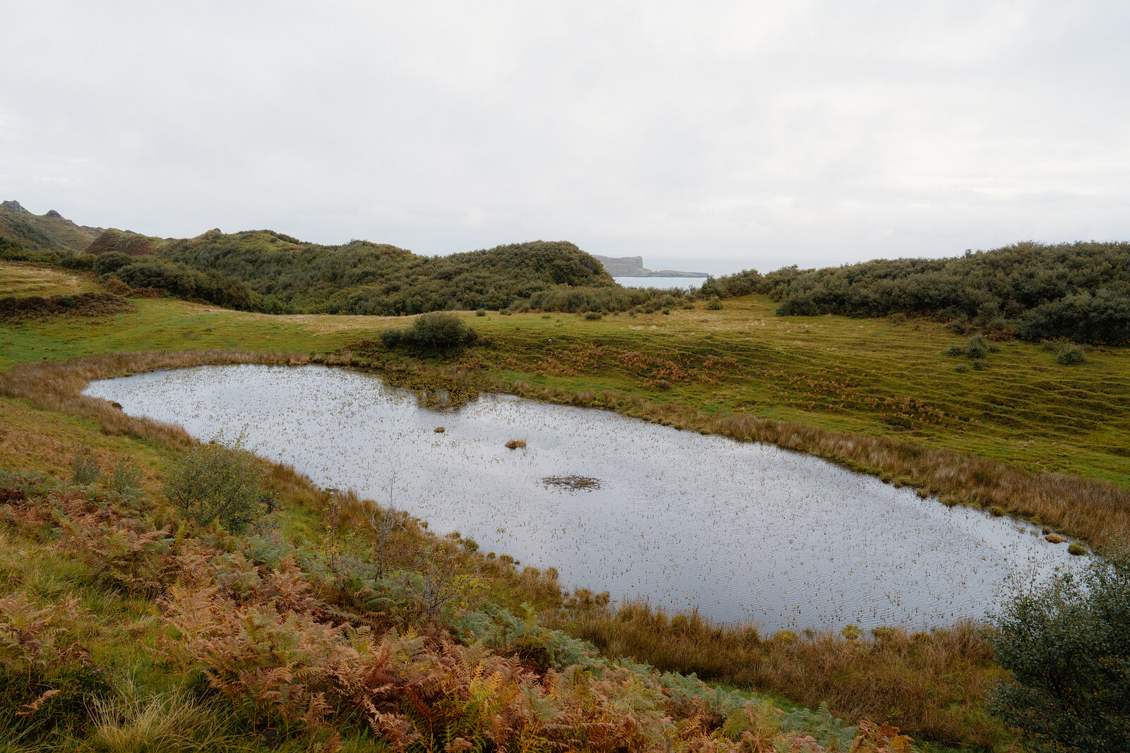 A small pond sits amid grassy dunes above the coastline on the Isle of Skye.