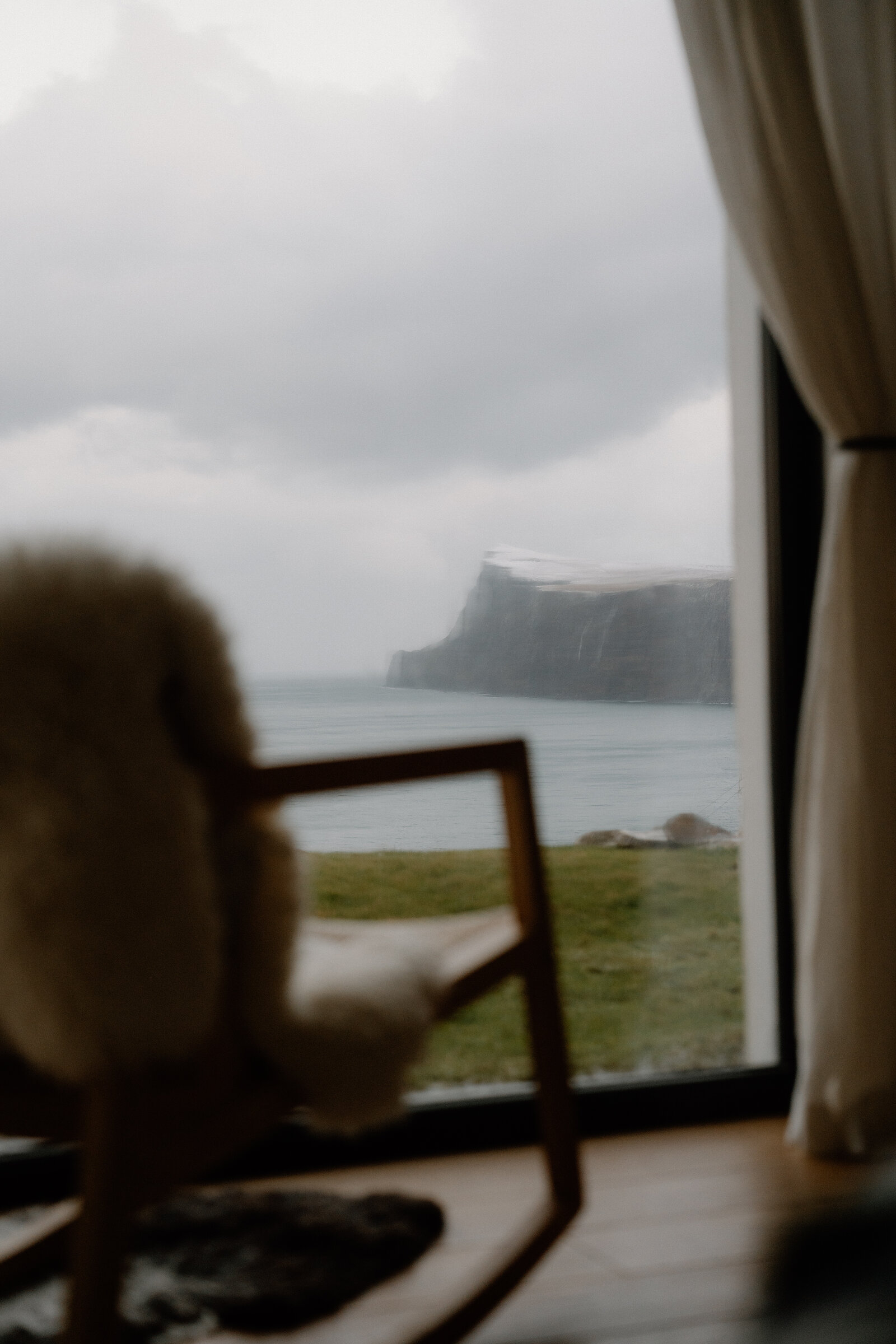A sheepskin-draped chair sits before a window overlooking cliffs and sea on the Isle of Skye.