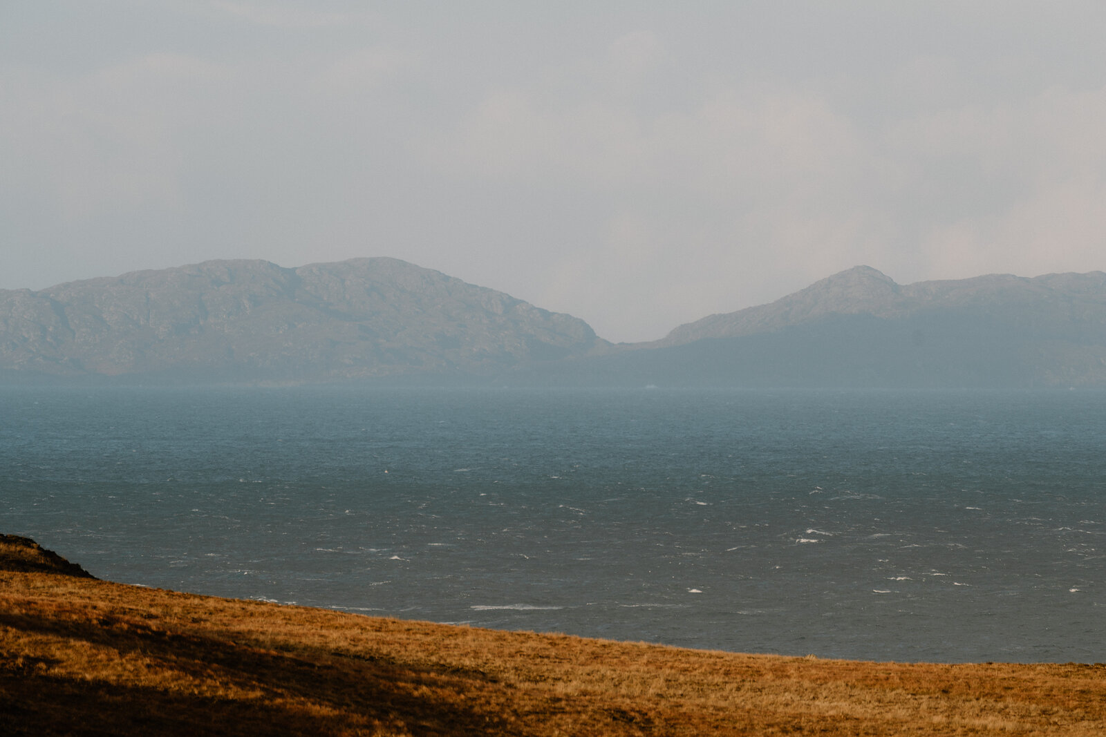 Distant hills rise across hazy water on the Isle of Skye.