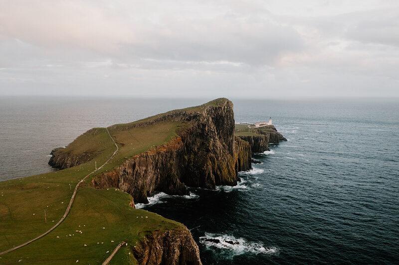 Neist Point Lighthouse stands beyond a narrow headland at dusk on the Isle of Skye.