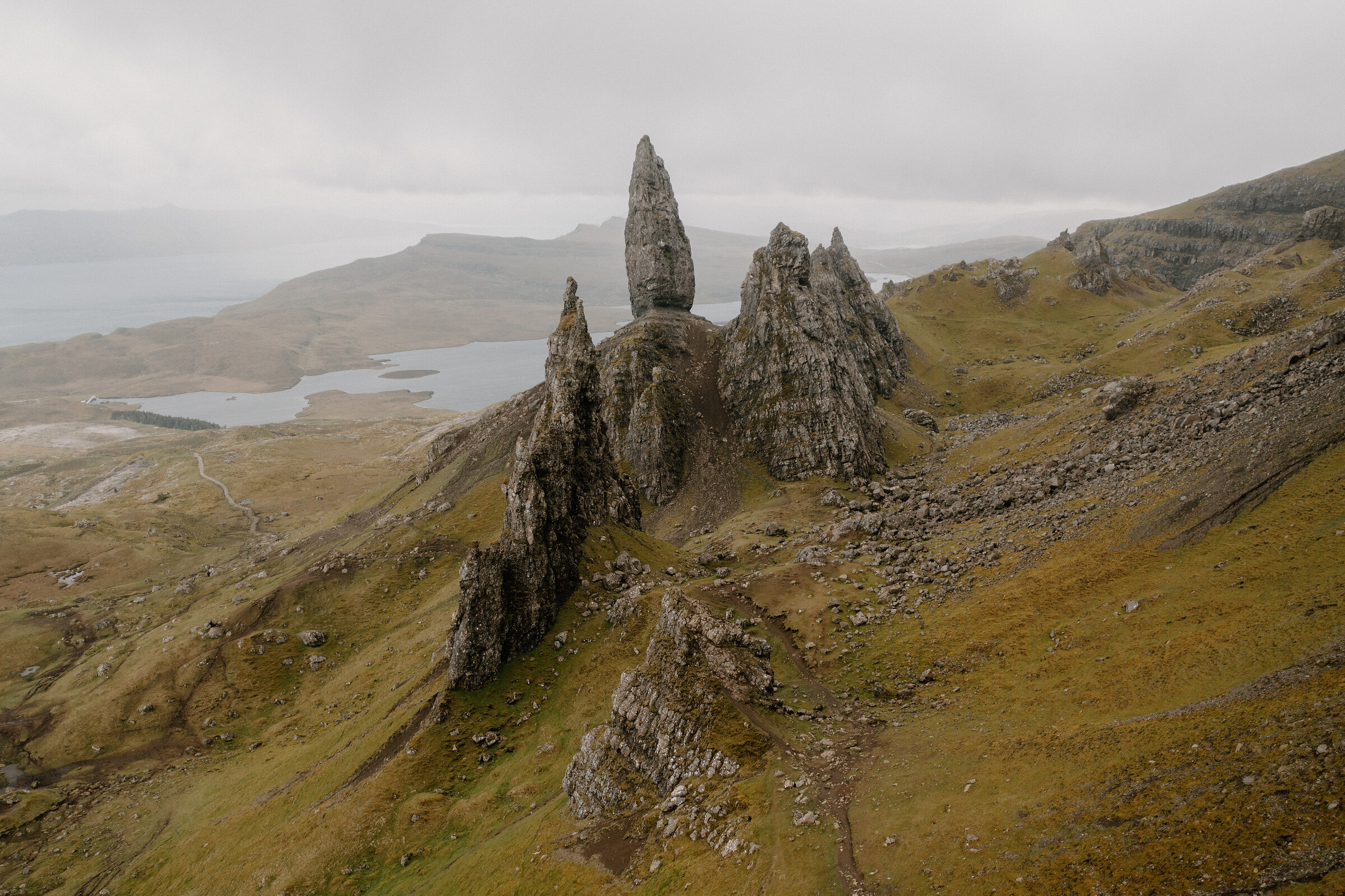 The Old Man of Storr's pinnacles rise above a hillside overlooking a loch and coastline on the Isle of Skye.