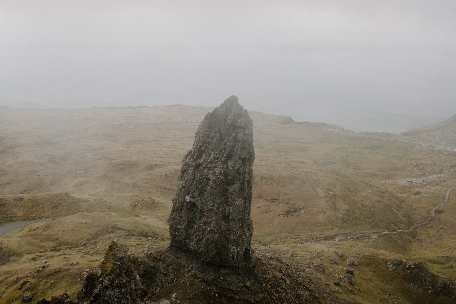 The Old Man of Storr's pinnacle rises through mist above a grassy hillside on the Isle of Skye.