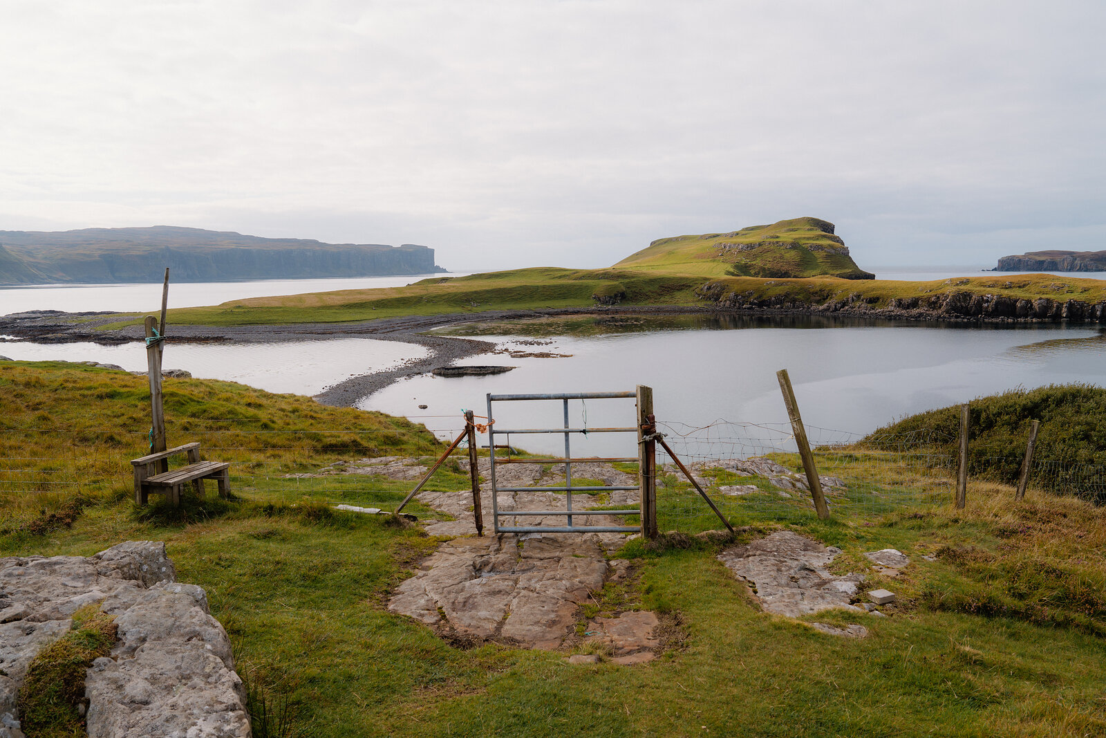 A metal gate stands before a grassy headland reaching into the sea on the Isle of Skye.