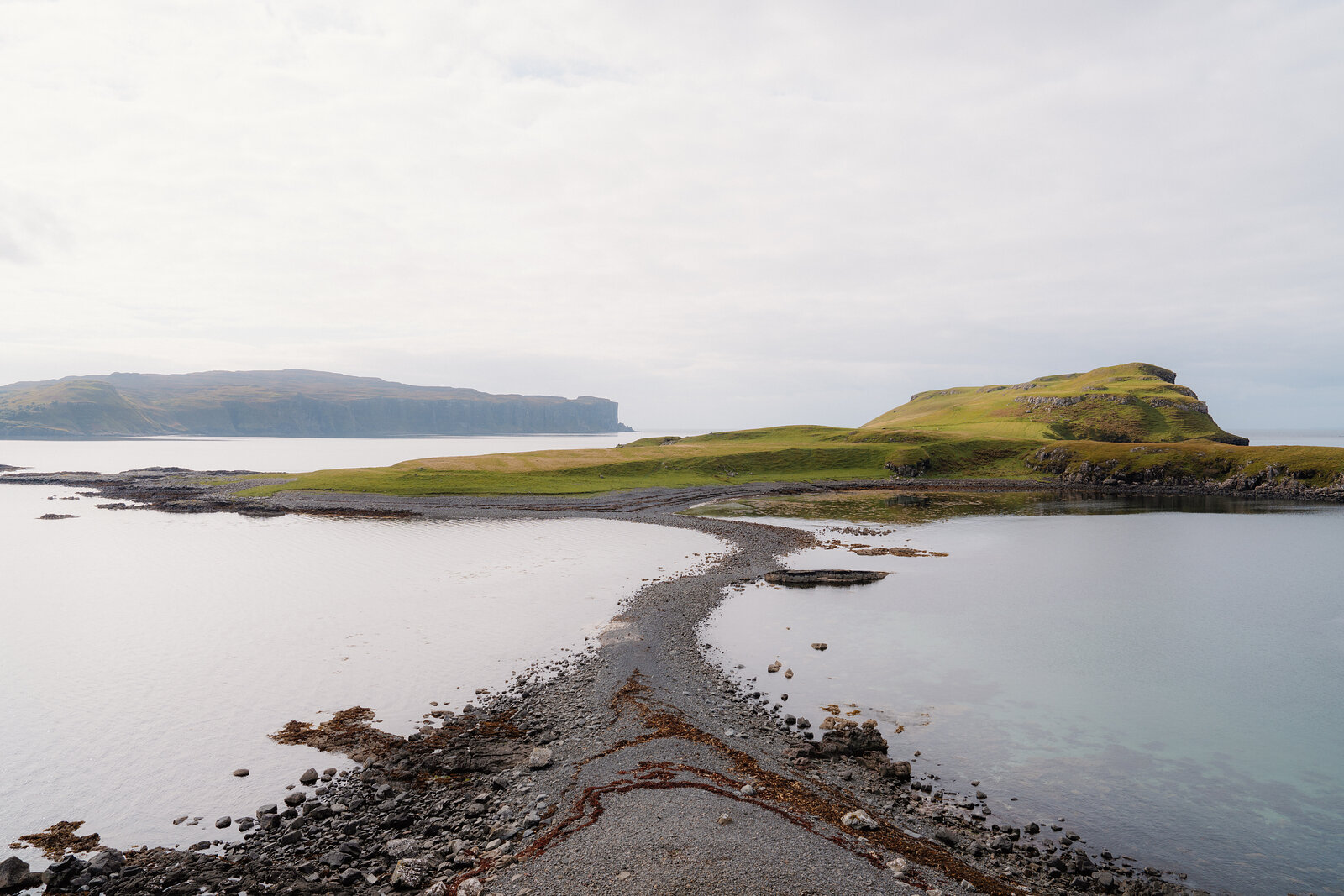 A shingle spit curves out to a grassy headland between two bays on the Isle of Skye.