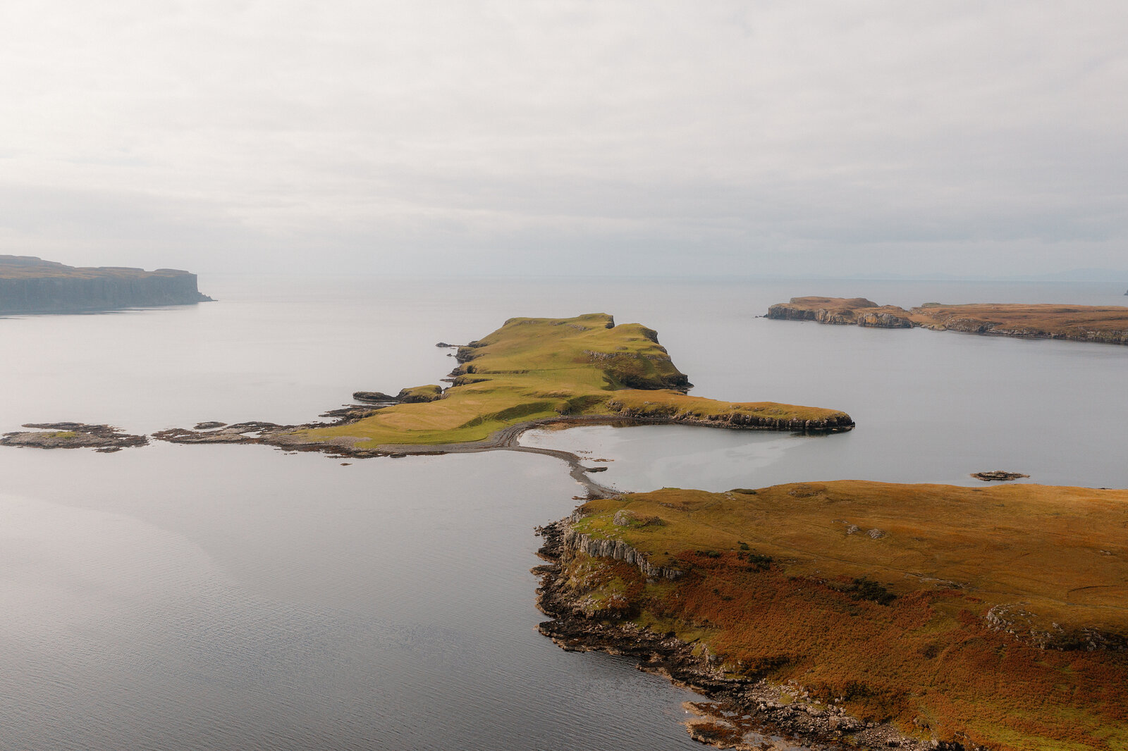 A grassy headland with dark cliffs juts into the sea, photographed from above on the Isle of Skye.