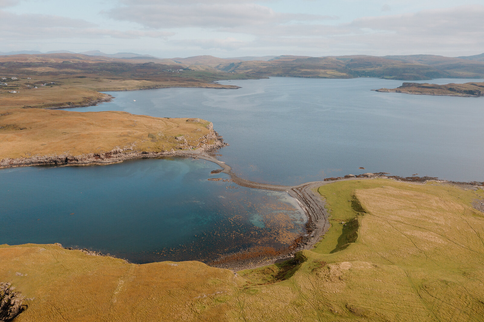 A calm bay curves past a grassy headland toward distant hills on the Isle of Skye.