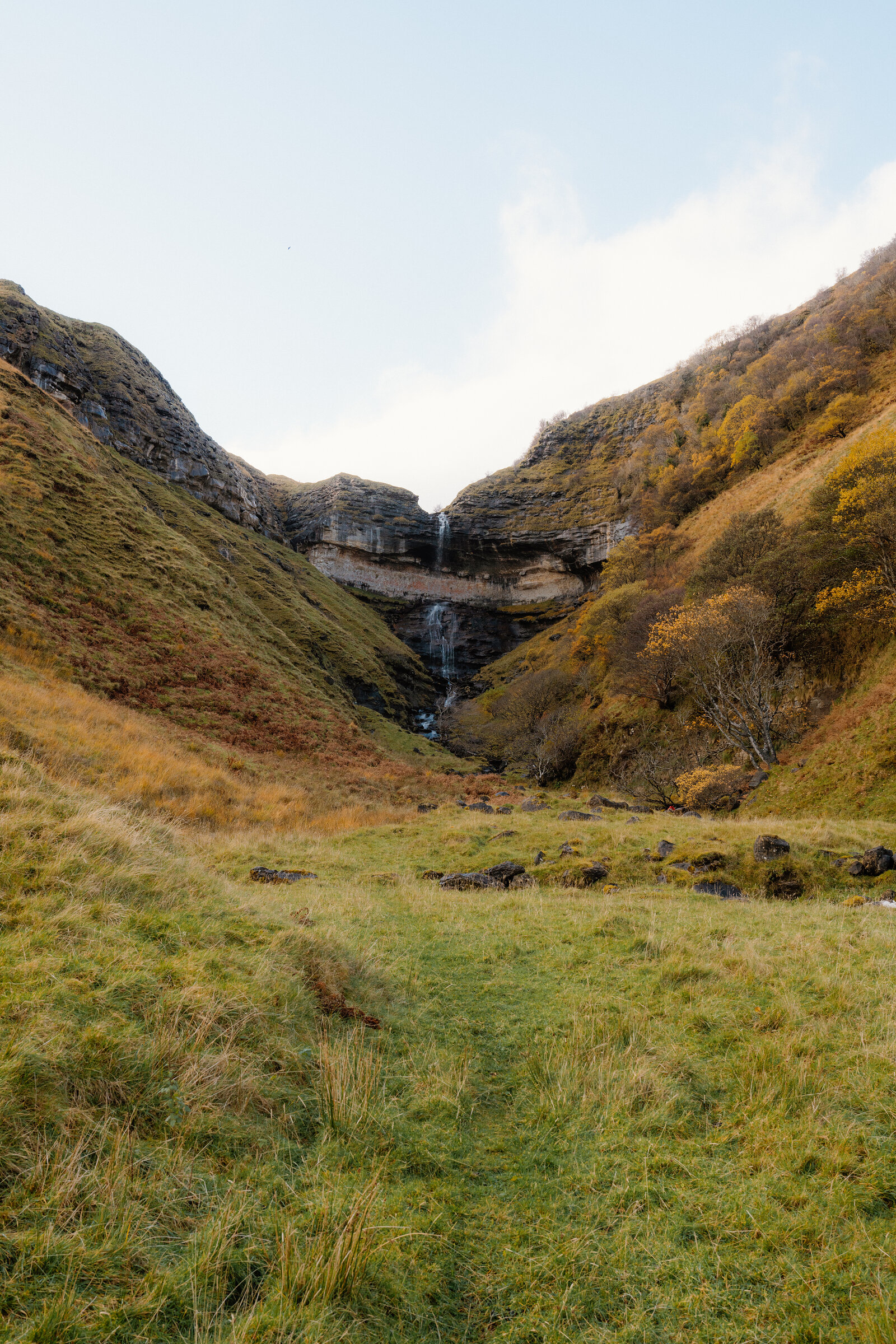 A waterfall tumbling down a rocky gorge between autumn-coloured hillsides