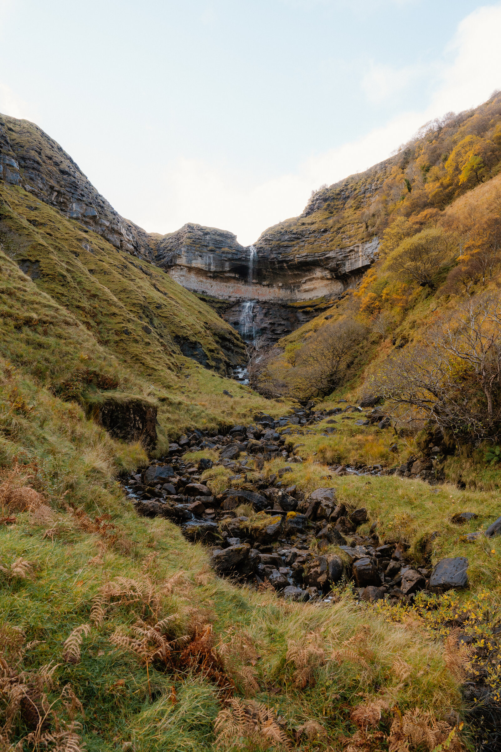 A waterfall tumbling down a rocky gorge between autumn-coloured hillsides