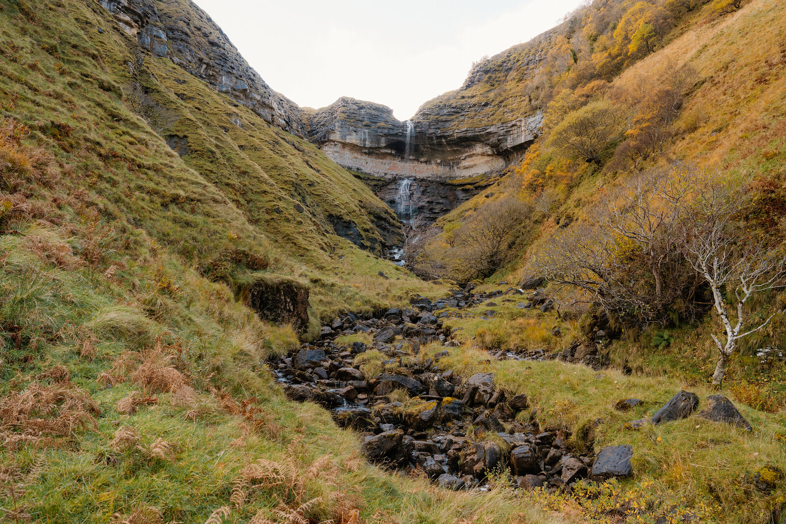 A waterfall tumbling down a rocky gorge between autumn-coloured hillsides