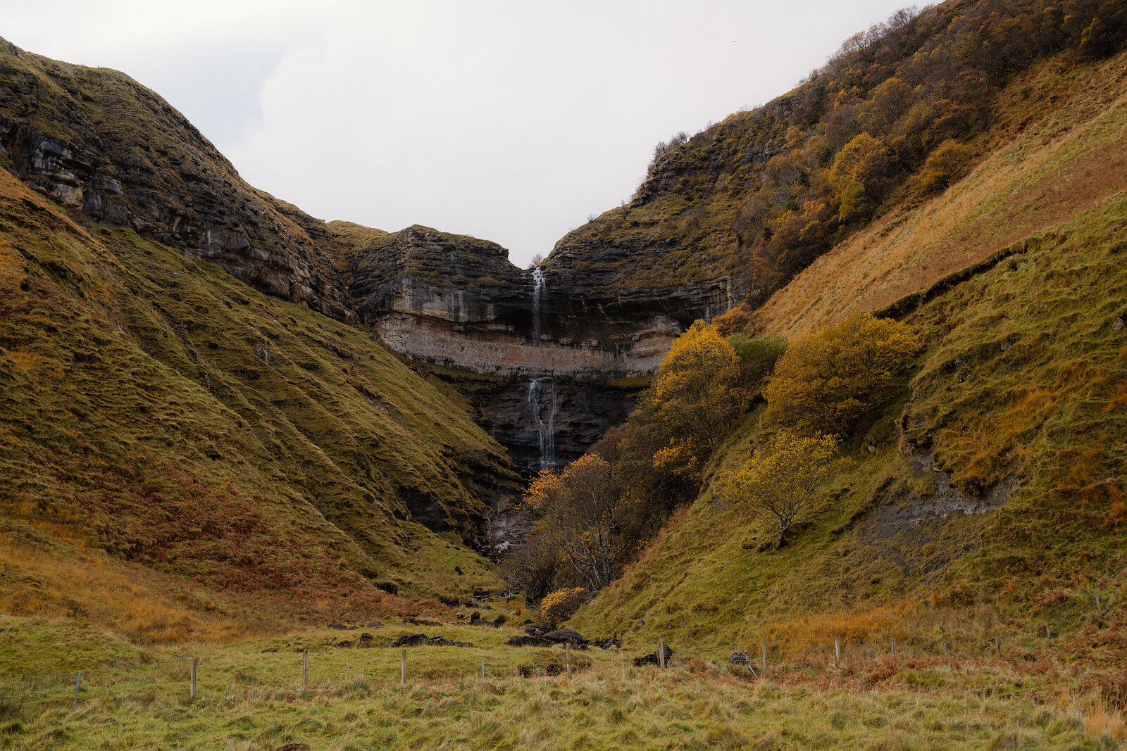 A waterfall dropping through a steep, autumn-coloured gorge between two hillsides