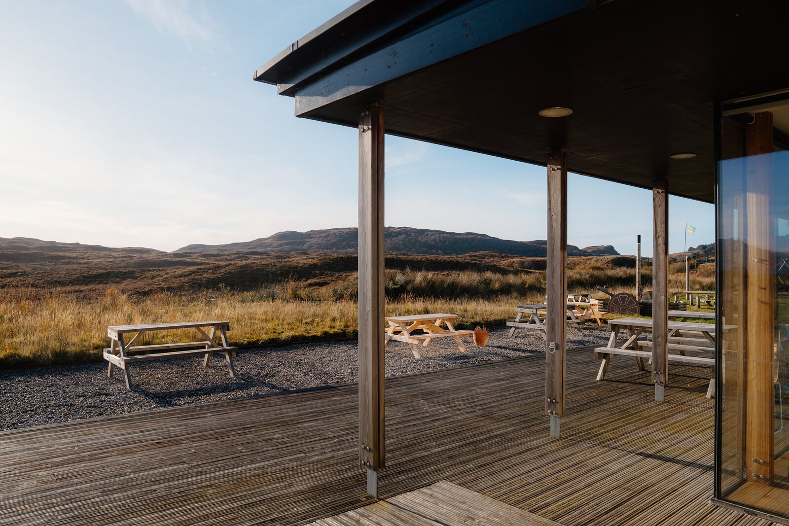 A covered timber decking area with picnic tables overlooking moorland and distant hills
