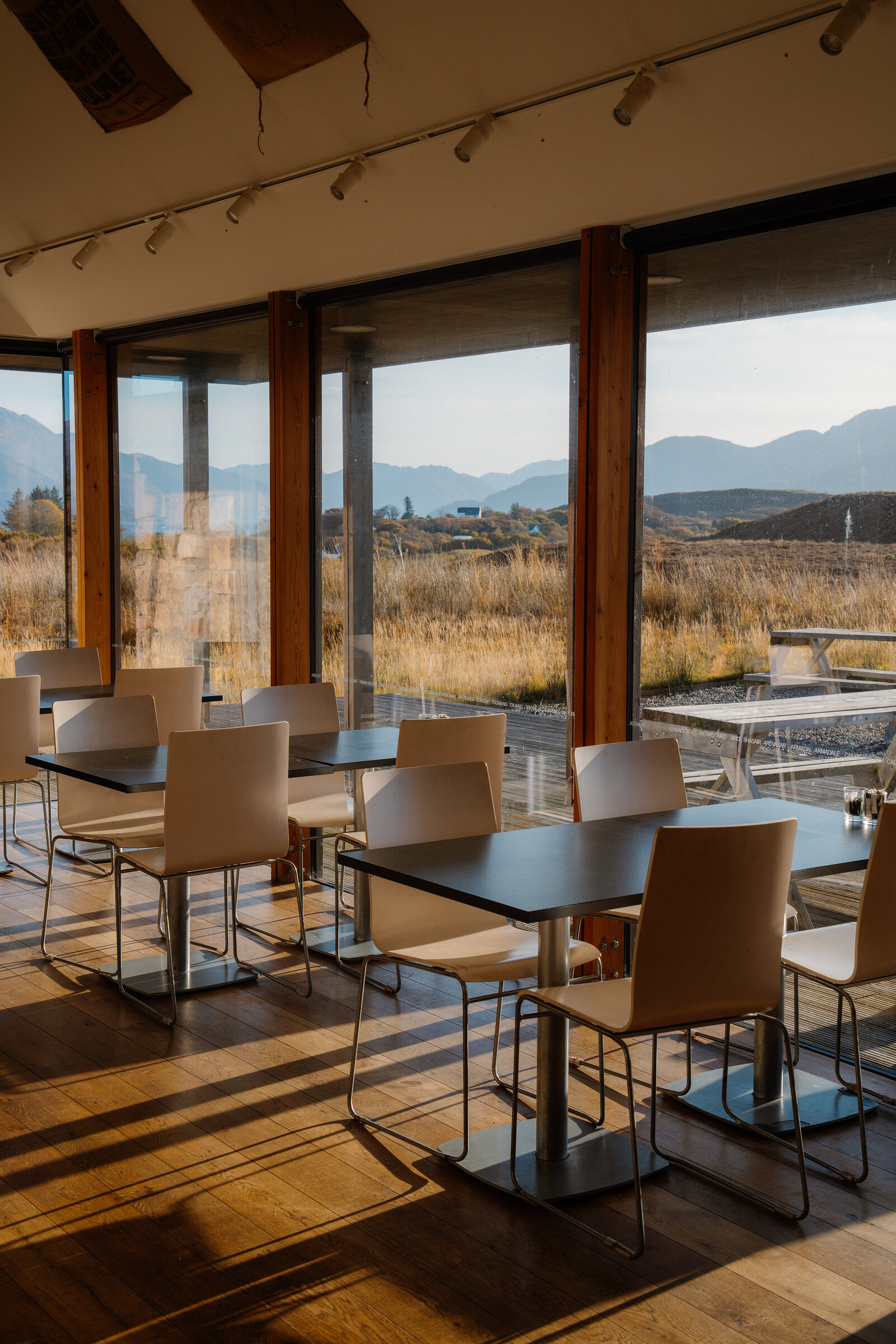 A dining room with tables and chairs set beside floor-to-ceiling windows overlooking hills and moorland
