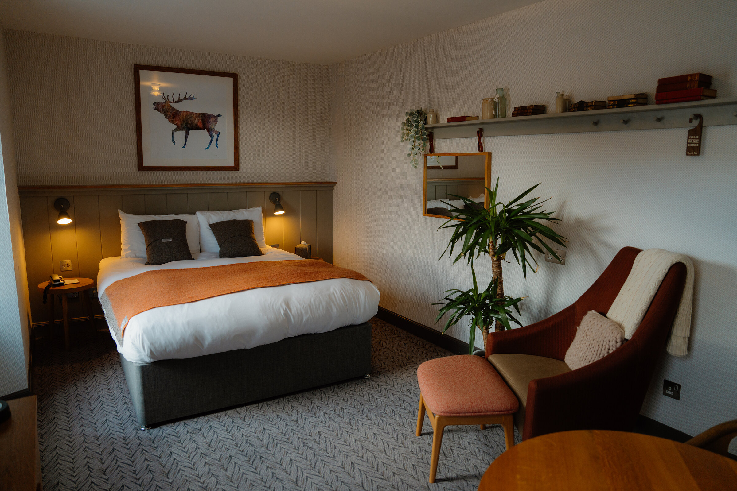 A stag print hangs above a bed dressed with orange cushions and a matching throw in a Bosville hotel room.