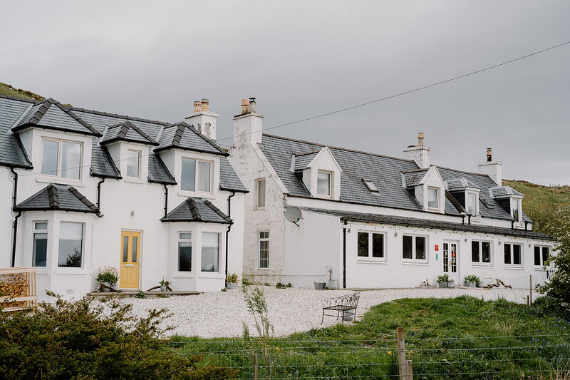 Coruisk House's white harled exterior shows dormer windows and clustered chimneys against a grey sky.