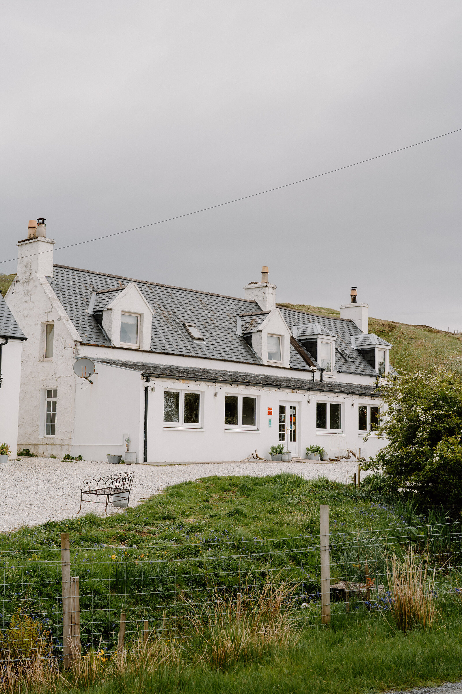 Coruisk House's long, single-storey white building has multiple dormer windows and chimneys along its slate roof.