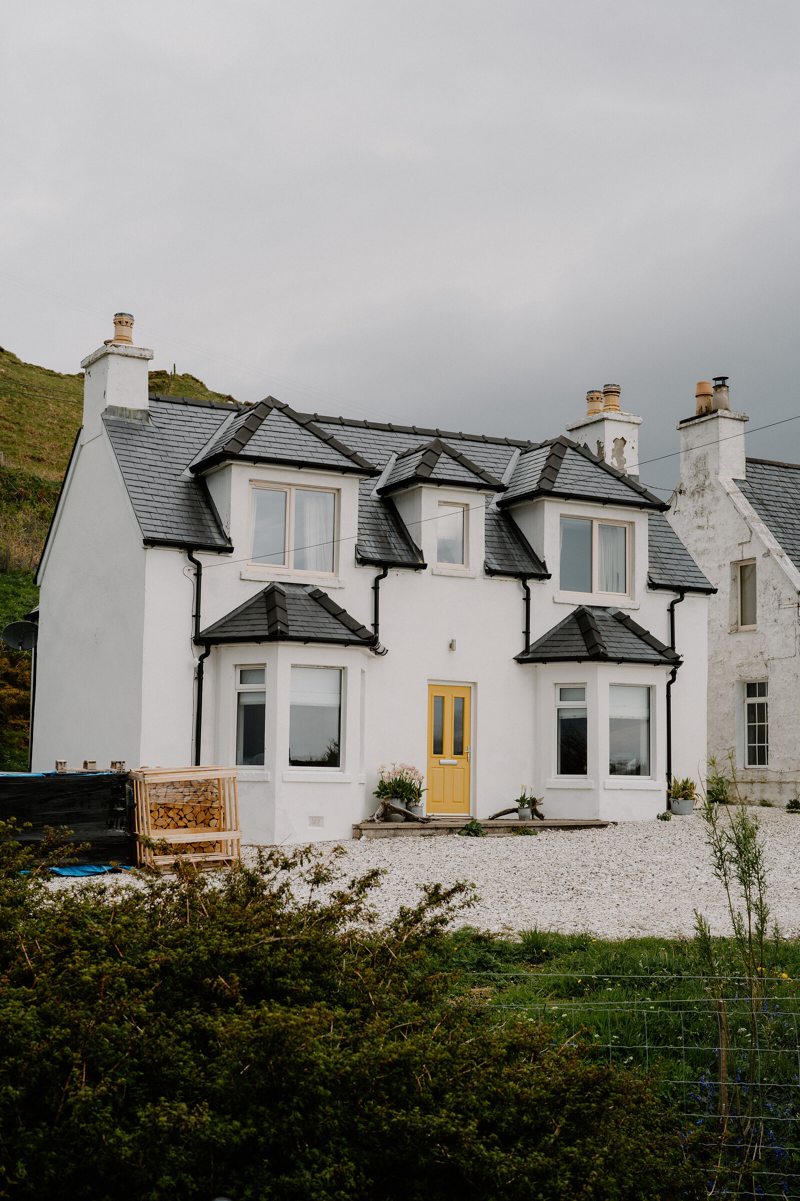 Coruisk House's white exterior features a yellow front door, dormer windows and a gravel driveway bordered by wire fencing.