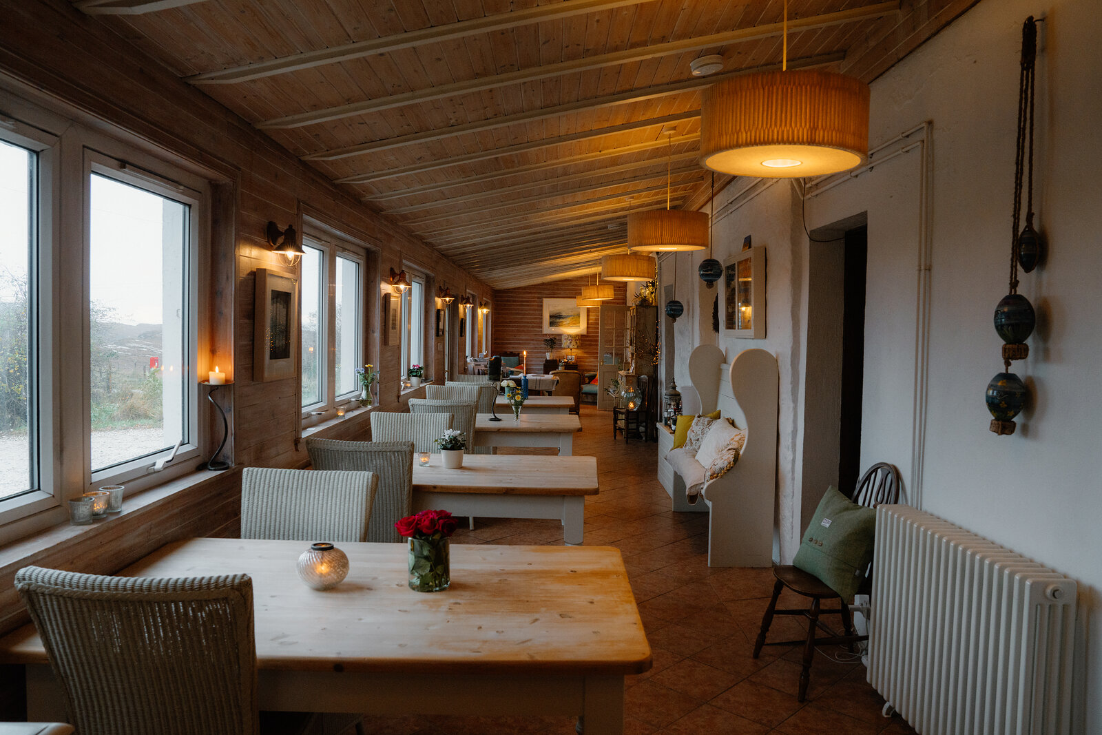Coruisk House's long dining room has a wood-panelled ceiling, hanging lampshades and tables set for a meal.