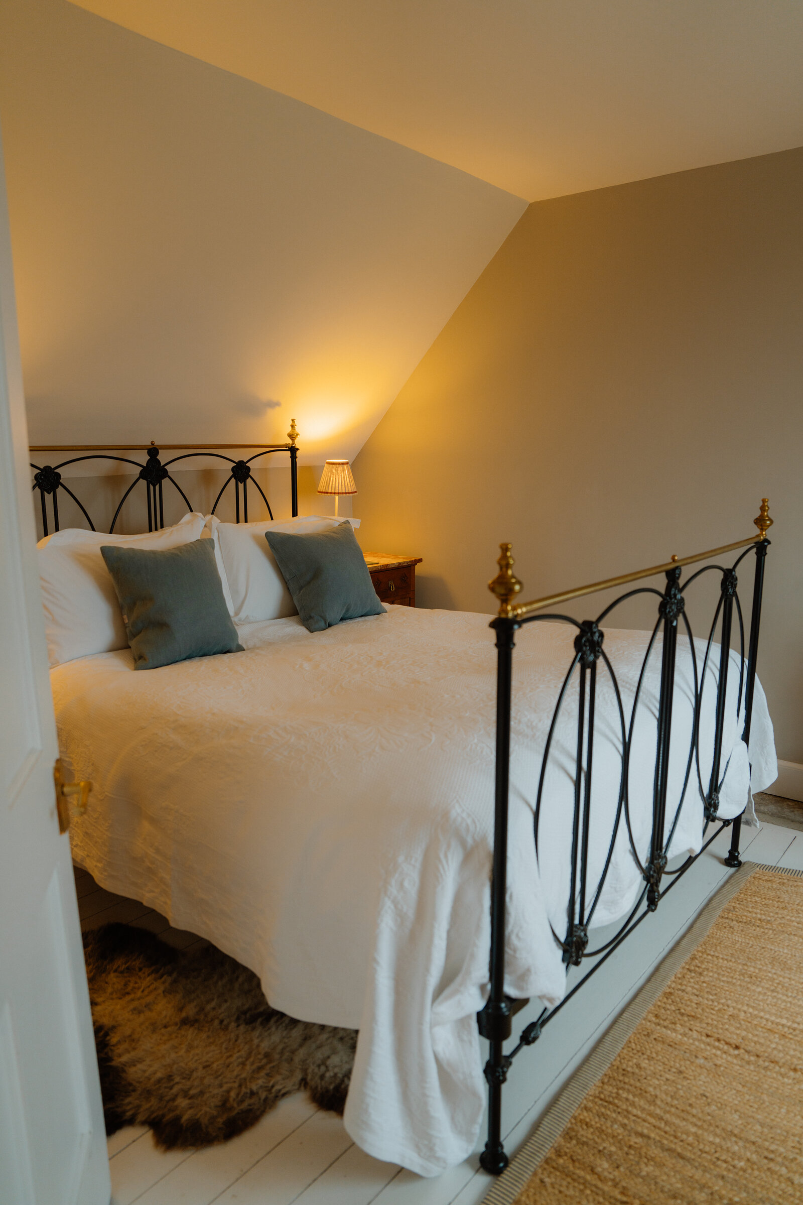 A wrought-iron bed with sage green cushions stands beneath a sloped ceiling in an attic bedroom at Coruisk House.